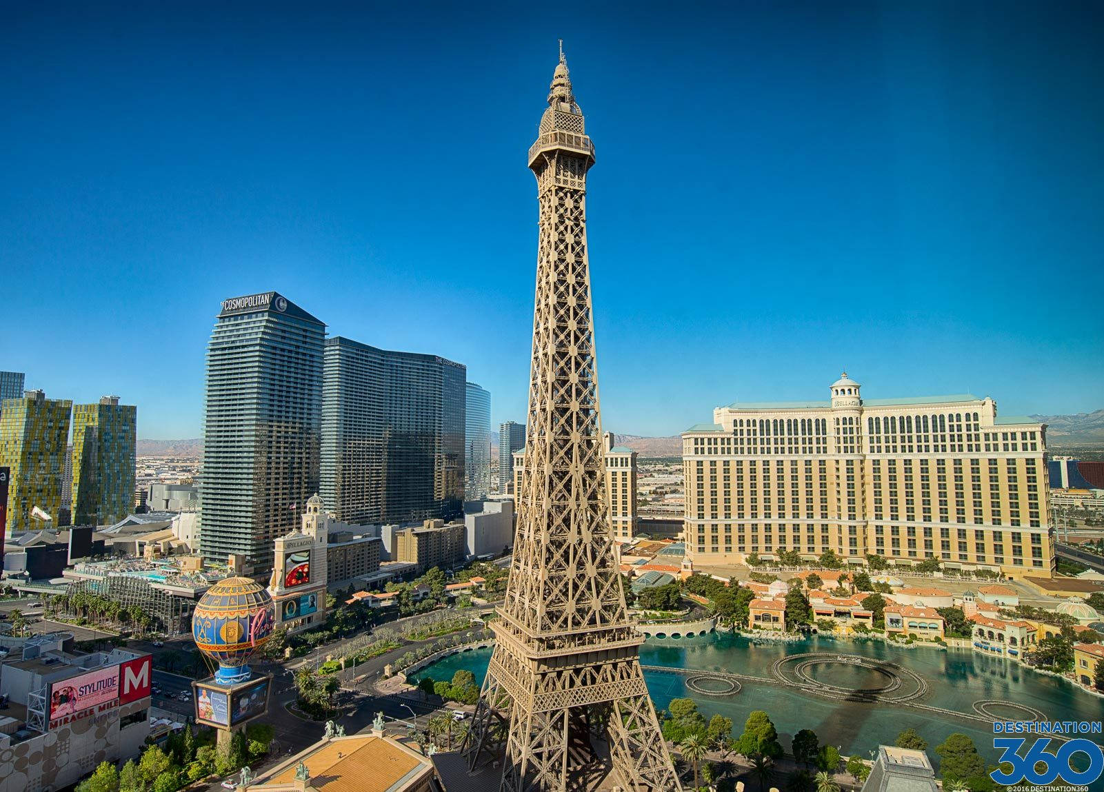 Eiffel Tower 桌布 壁紙 — 一座高聳的艾菲爾鐵塔複製品矗立在拉斯維加斯的心臟地帶，映襯著清澈的藍天，周圍環繞著標誌性酒店和繁華的城市景觀。