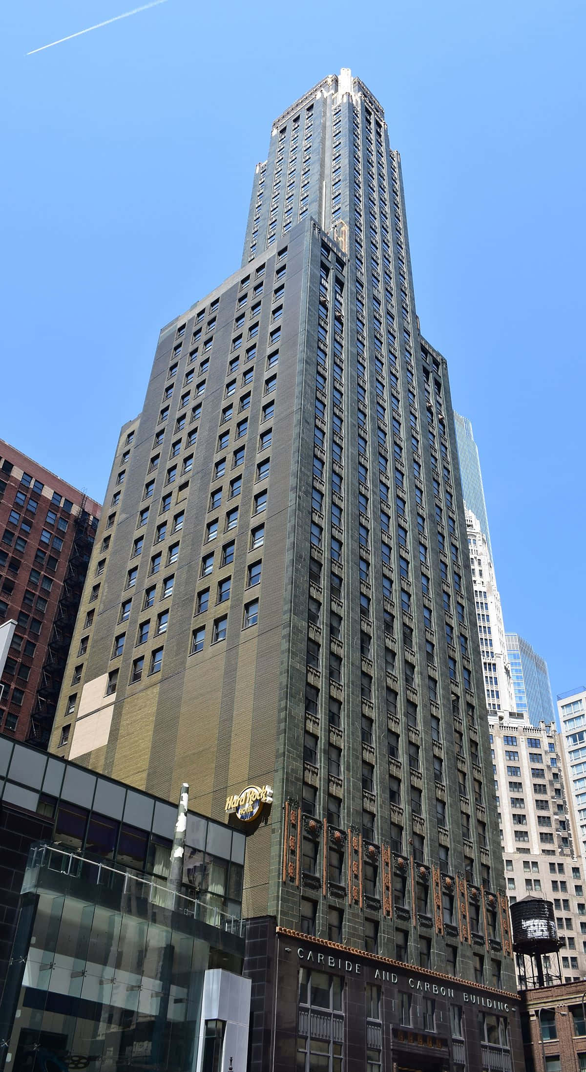 Buildings 桌布 壁紙 — 一座高聳的裝飾藝術風格摩天大樓，採用深色石材和華麗細節，在繁忙的城市環境中聳立於清澈的藍天下。