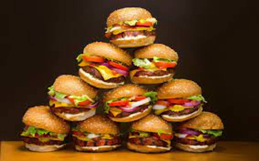 Burger King 桌布 壁紙 — 一座高聳的起司漢堡金字塔，堆疊在木質表面上，背景為深色。