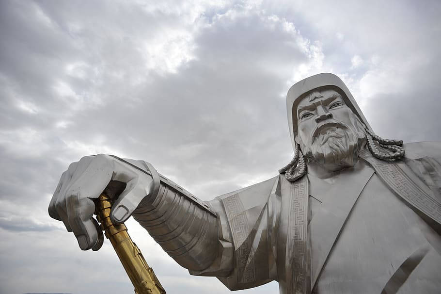 雲朵 桌布 壁紙 — 一座高聳的金屬成吉思汗雕像，手持金色權杖，背景是戲劇性的多雲天空。