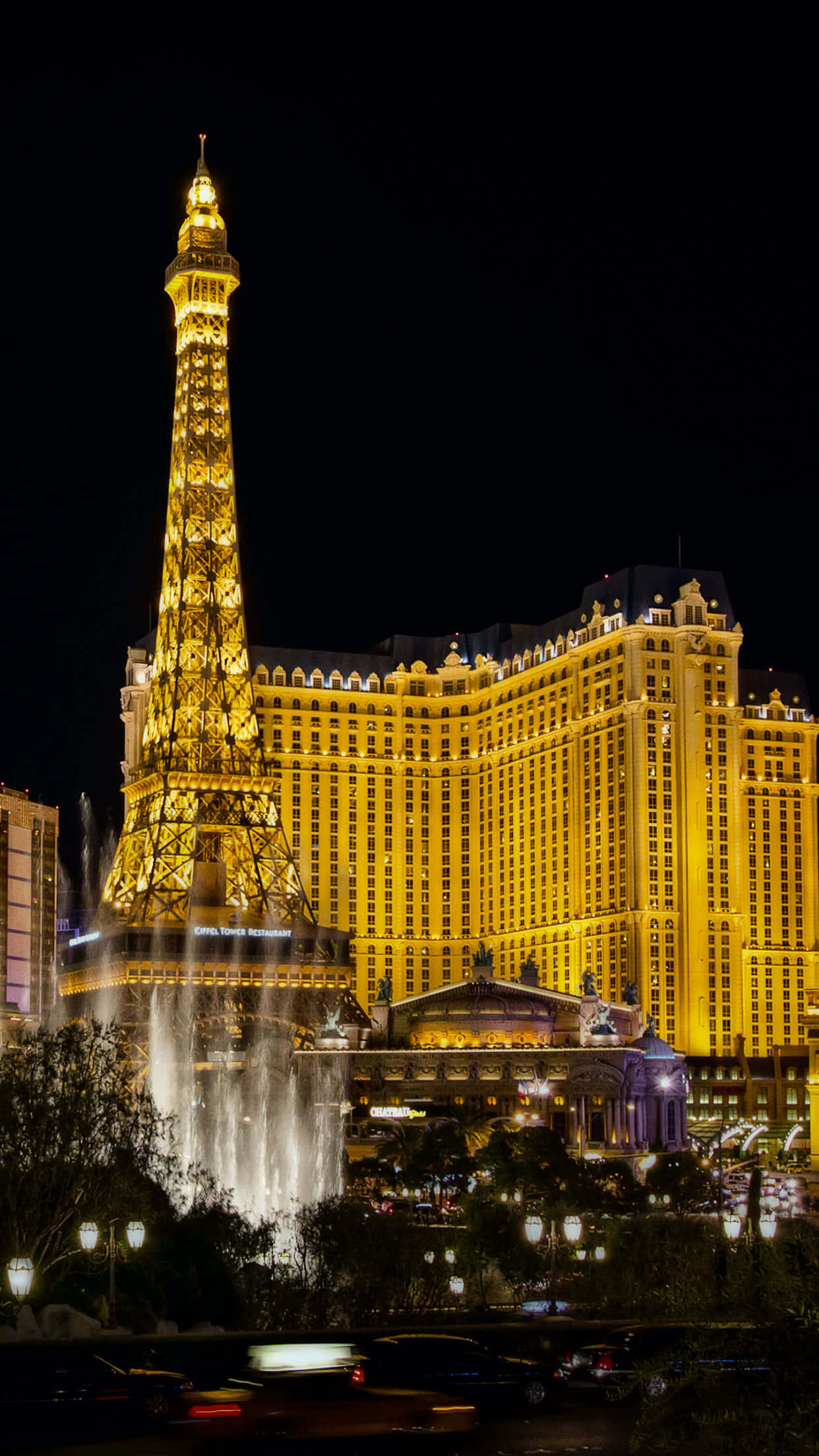 Las Vegas 桌布 壁紙 — 一座高聳的金色艾菲爾鐵塔複製品在夜間亮起，旁邊是一座擁有層疊噴泉和閃爍燈光的豪華酒店。