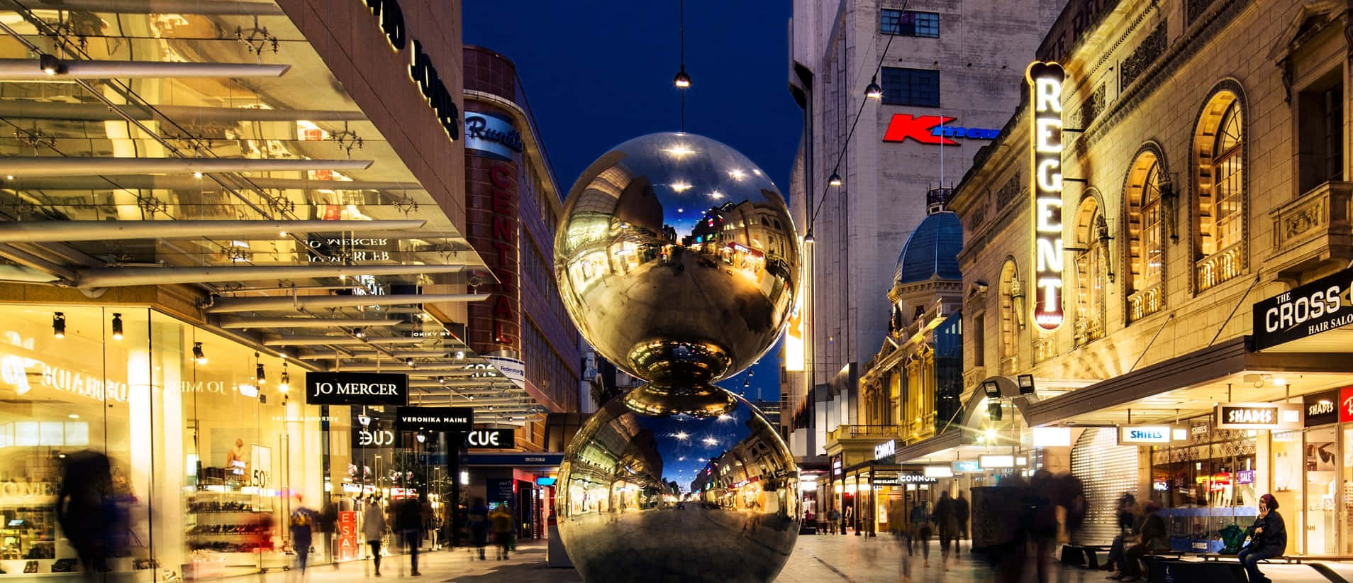 Adelaide 桌布 壁紙 — 一座高聳的鉻球雕塑在暮色中反射著繁忙城市街道上的霓虹燈光和模糊的行人。