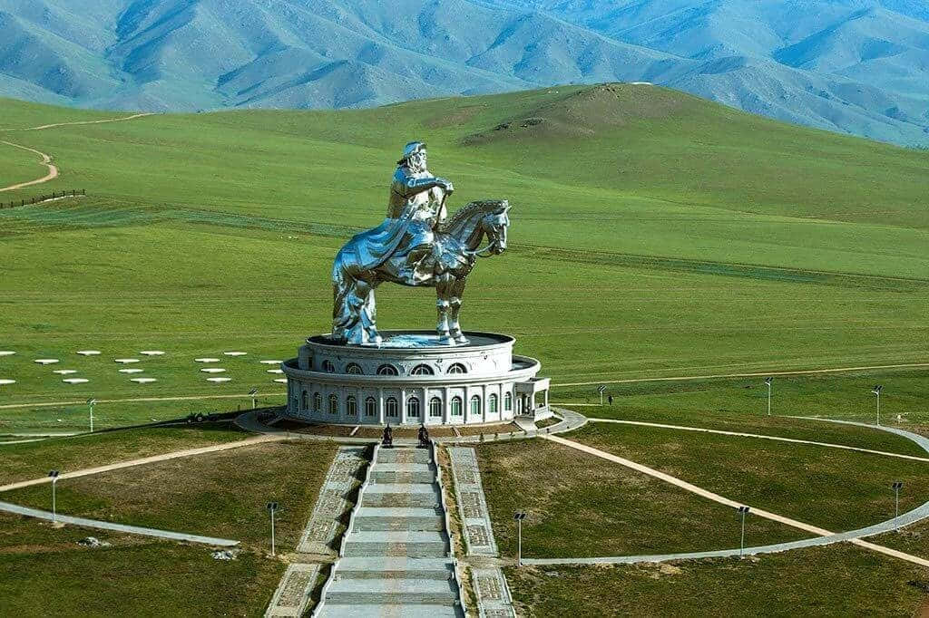 風景 桌布 壁紙 — 一座高聳的銀色騎馬雕像矗立在圓形基座上，背景是廣闊的綠色山谷和連綿起伏的山脈。