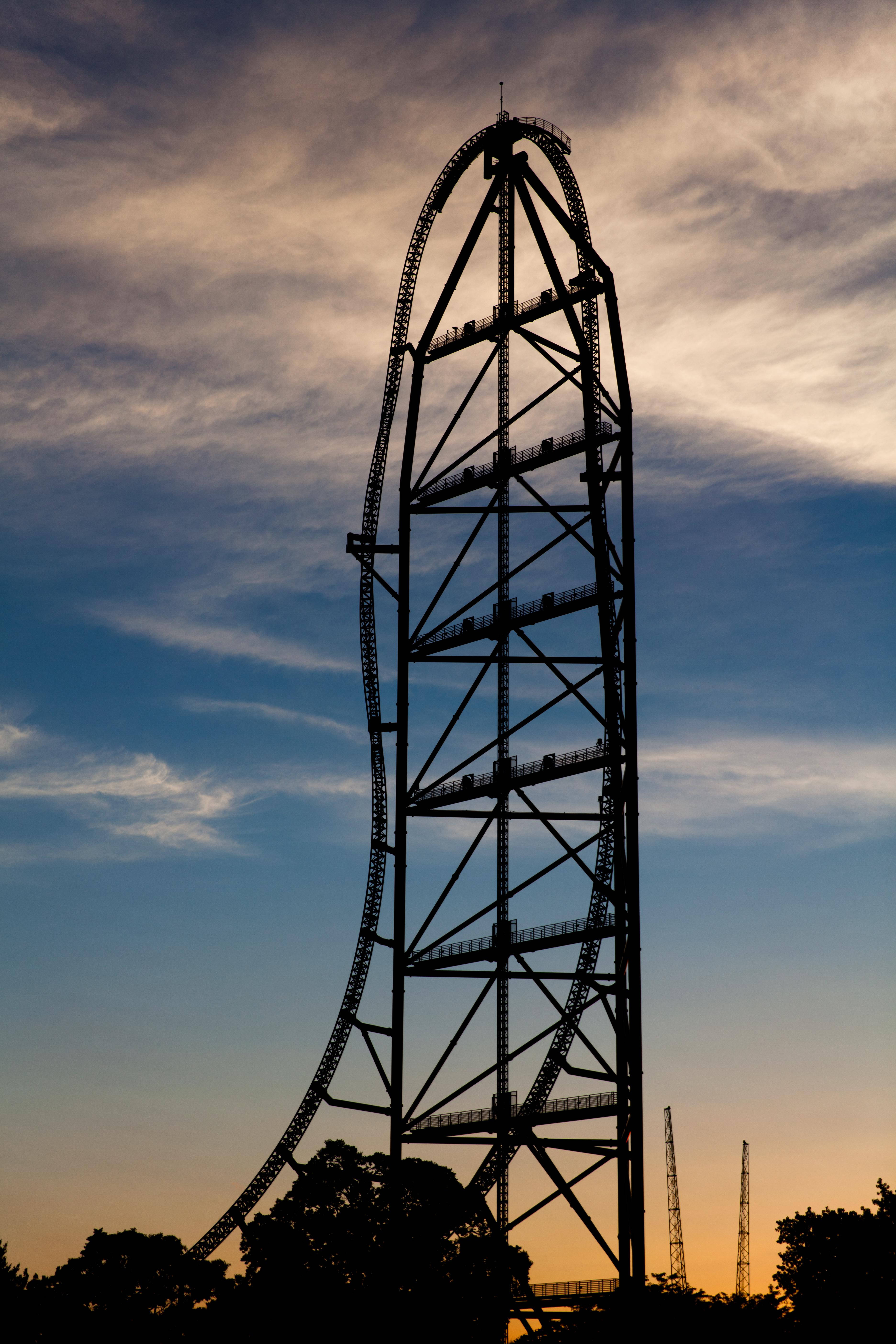 Roller Coaster 桌布 壁紙 — 一座高聳的雲霄飛車在暮色天空下呈現剪影，天空帶有橙色和藍色的雲彩條紋。