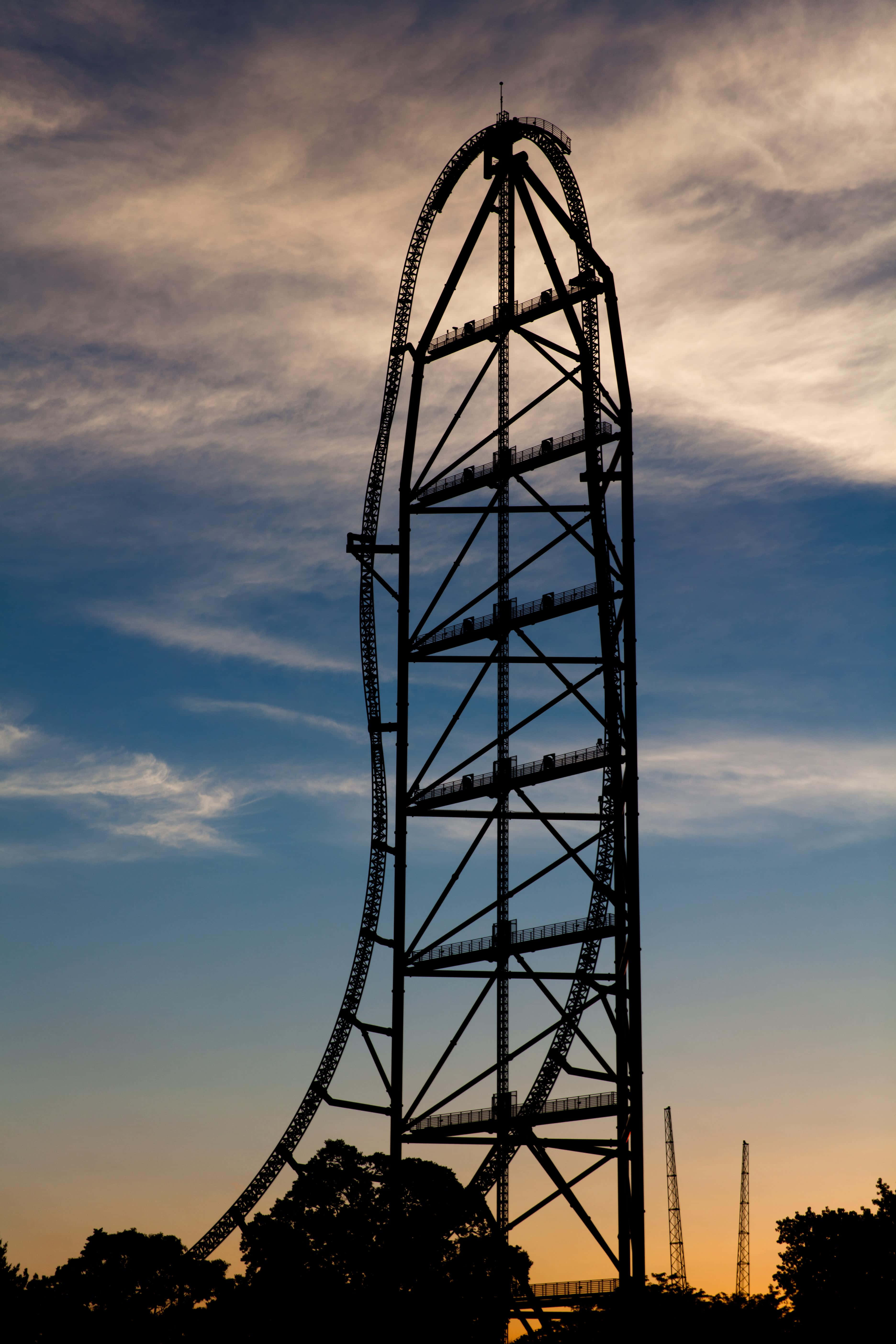 Roller Coaster 桌布 壁紙 — 一座高聳的雲霄飛車在黃昏天空的襯托下呈現剪影，天空帶有橙色和藍色的雲彩條紋。