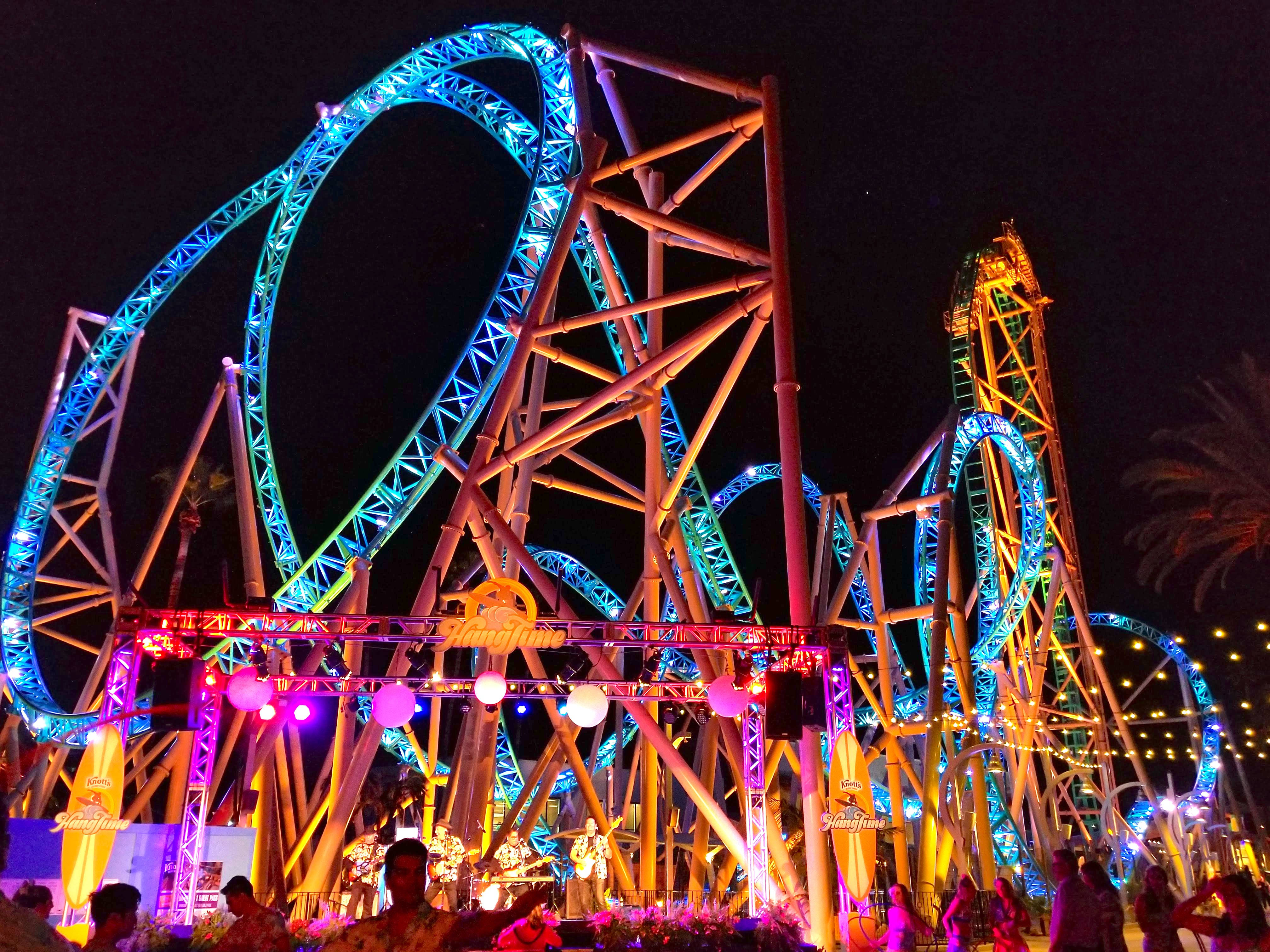 Roller Coaster 桌布 壁紙 — 一座高聳的雲霄飛車被鮮豔的藍色和紫色燈光照亮，主宰著夜間遊樂園場景，下方是剪影般的人群。