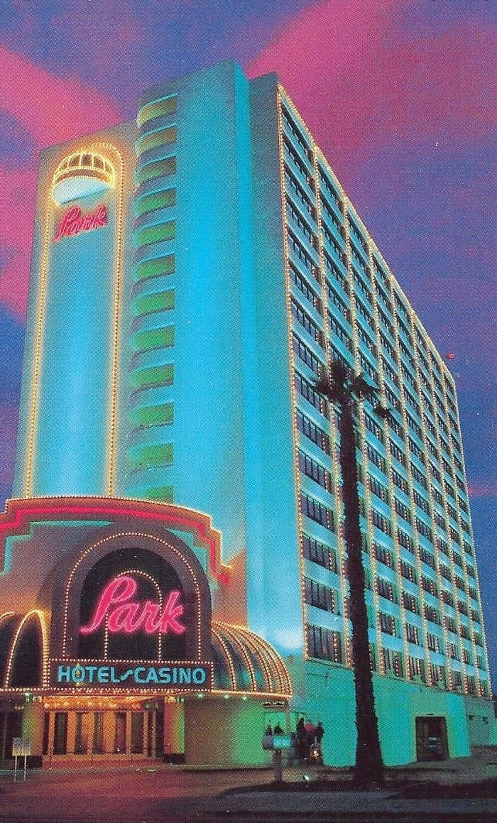 Hotel 桌布 壁紙 — 一座高聳的霓虹燈酒店賭場建築在暮色天空下閃耀著藍綠色和粉紅色，附近有棕櫚樹的剪影。