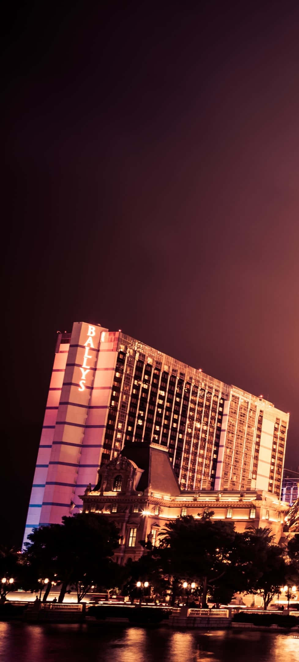 Las Vegas Phone 桌布 壁紙 — 一座高聳的飯店，帶有粉紅色霓虹燈點亮的「BALYS」字樣，在漆黑的夜空下熠熠生輝，燈光倒映在下方平靜的水面上。