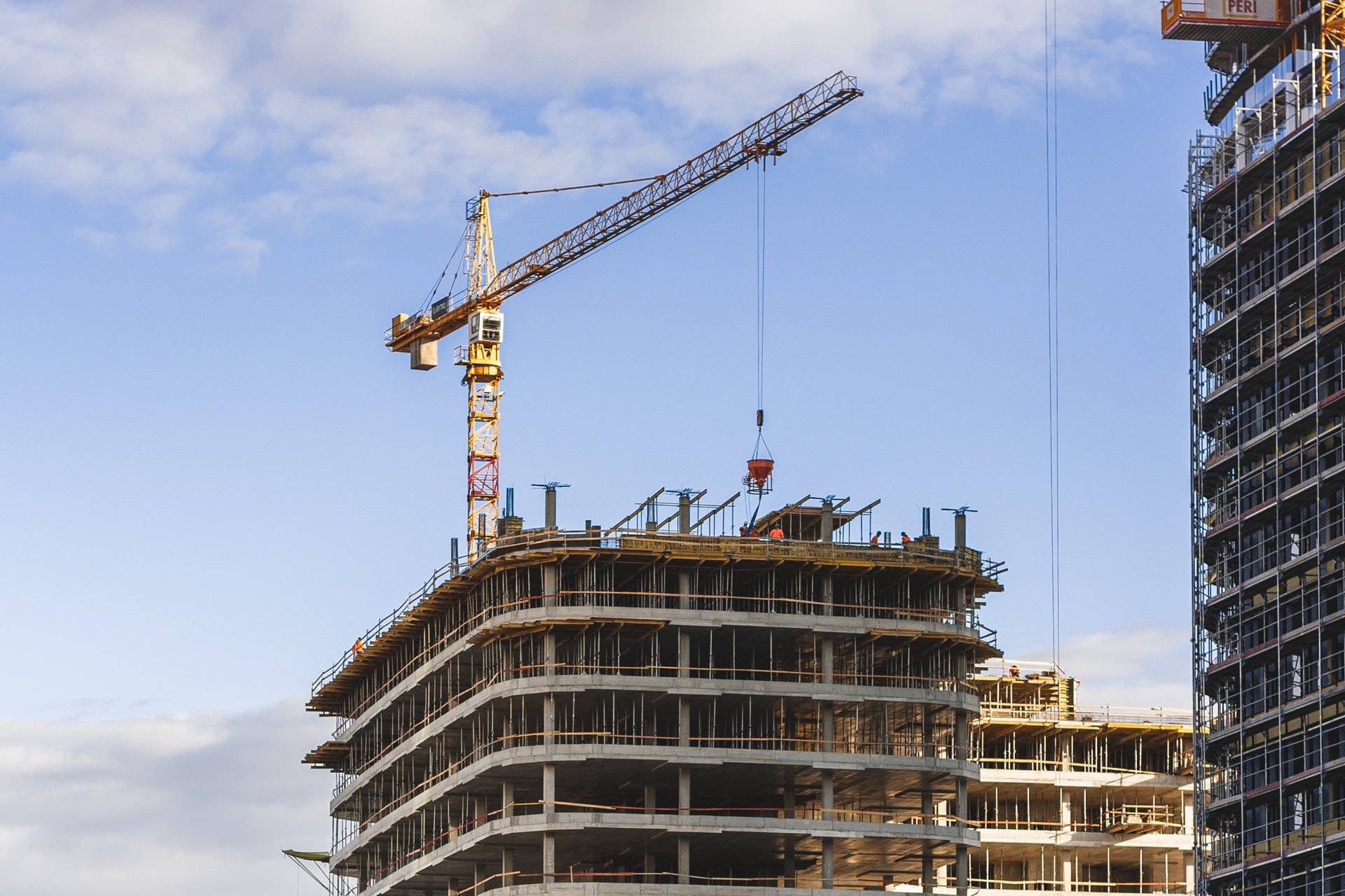 engineering 桌布 壁紙 — 一座高聳的黃色起重機在建築中的多層混凝土建築上方吊運材料，背景是明亮的藍天和零星白雲。