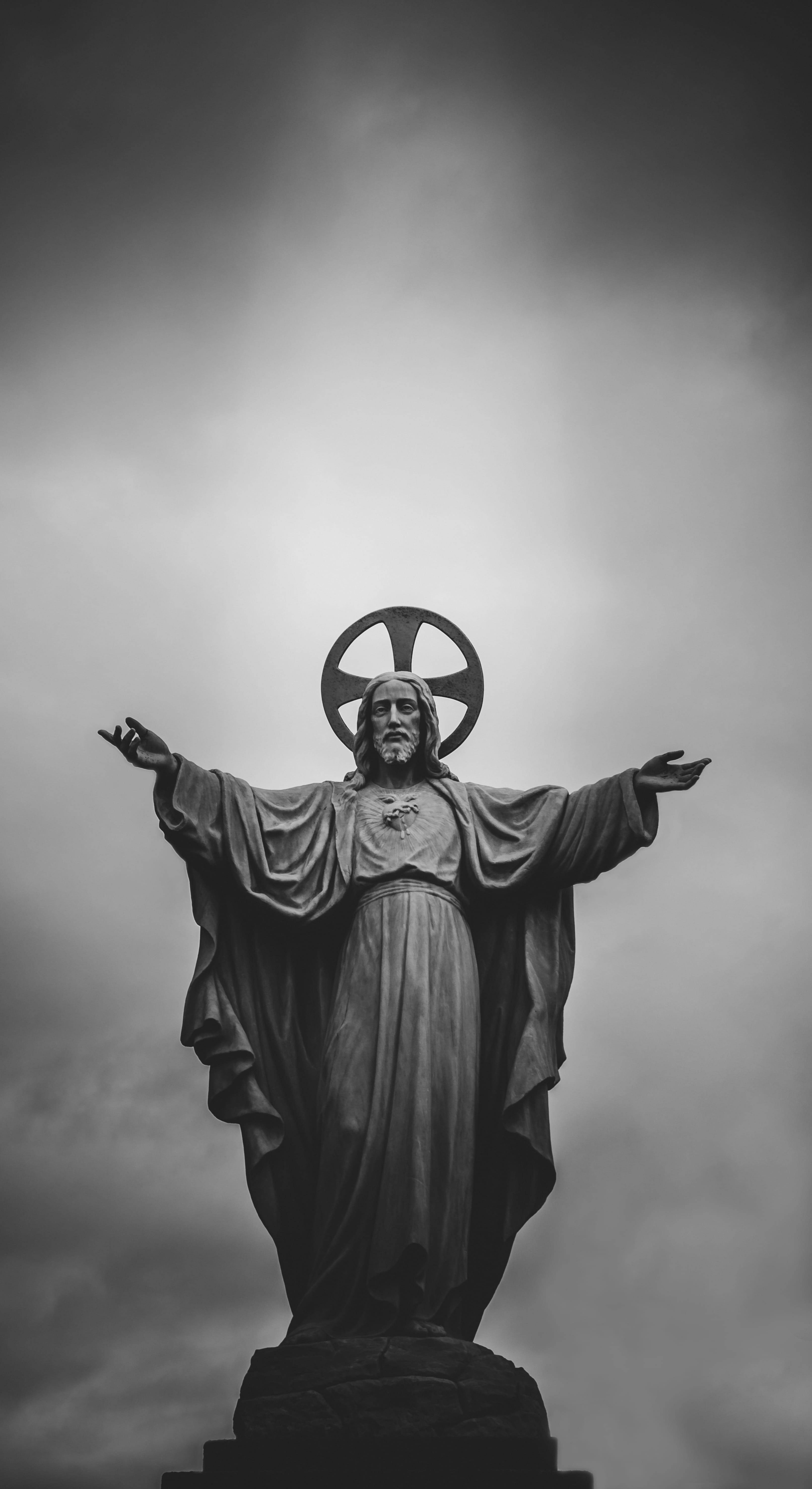 Christ 桌布 壁紙 — 一座高聳的黑白耶穌雕像，雙臂張開，頭頂光環，矗立在戲劇性的多雲天空下。