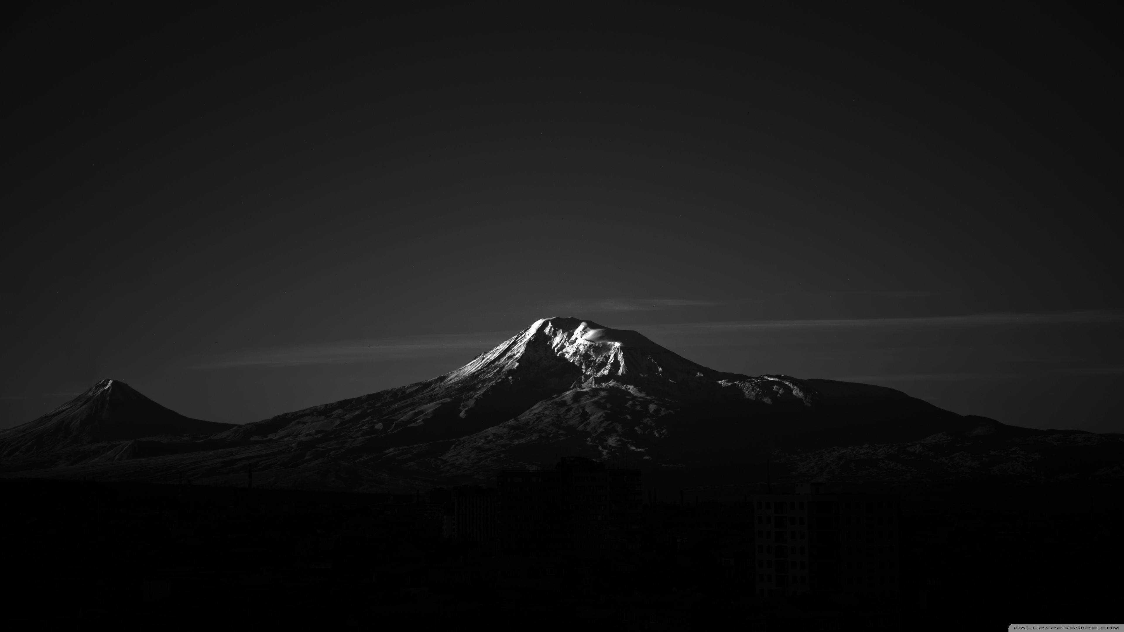 黑白 桌布 壁紙 — 一座鮮明的黑白山峰剪影，積雪的山頂在黑暗的天空中閃耀。