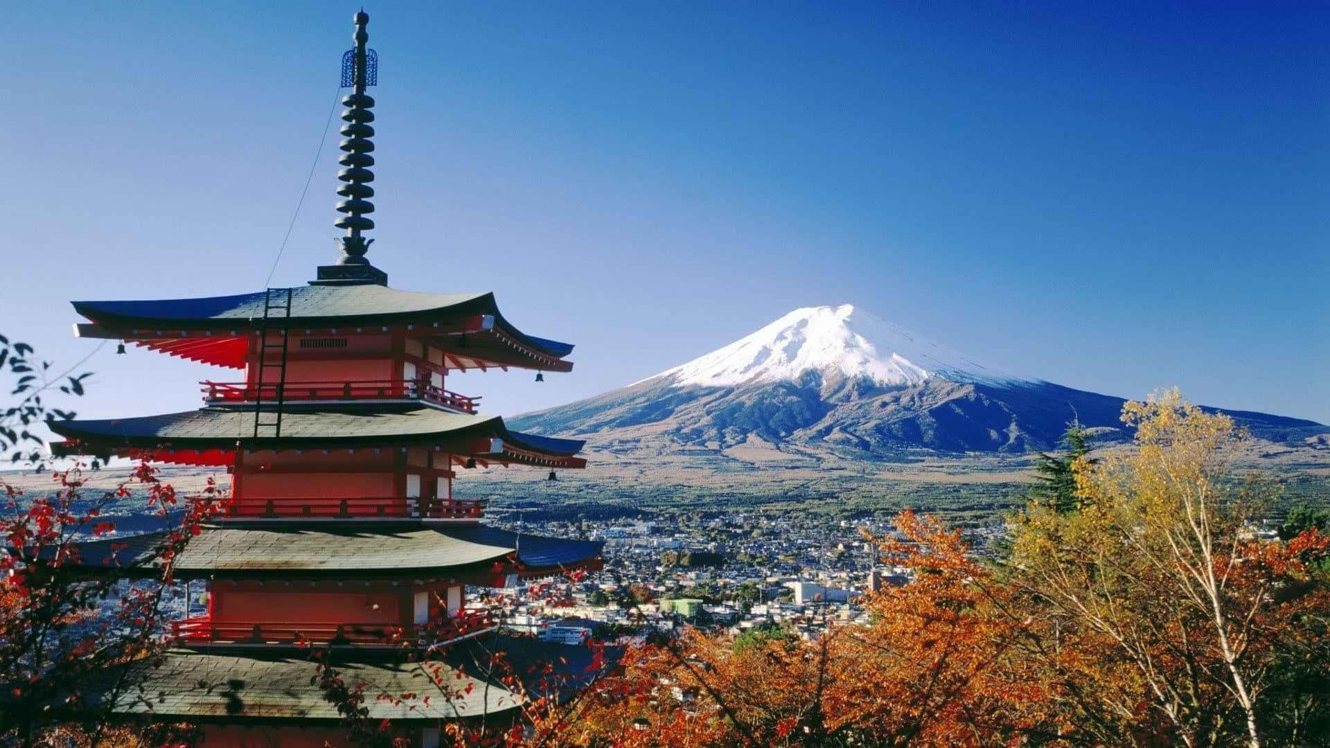 桌布 壁紙 — 一座鮮紅色的日本寶塔矗立在富士山白雪皚皚的山峰前，藍天白雲，秋葉環繞。
