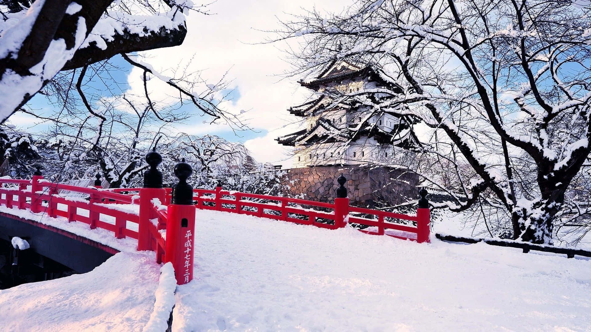 Best Winter 桌布 壁紙 — 一座鮮紅色的橋樑通往一座被雪覆蓋的日本城堡，天空湛藍，樹木光禿。