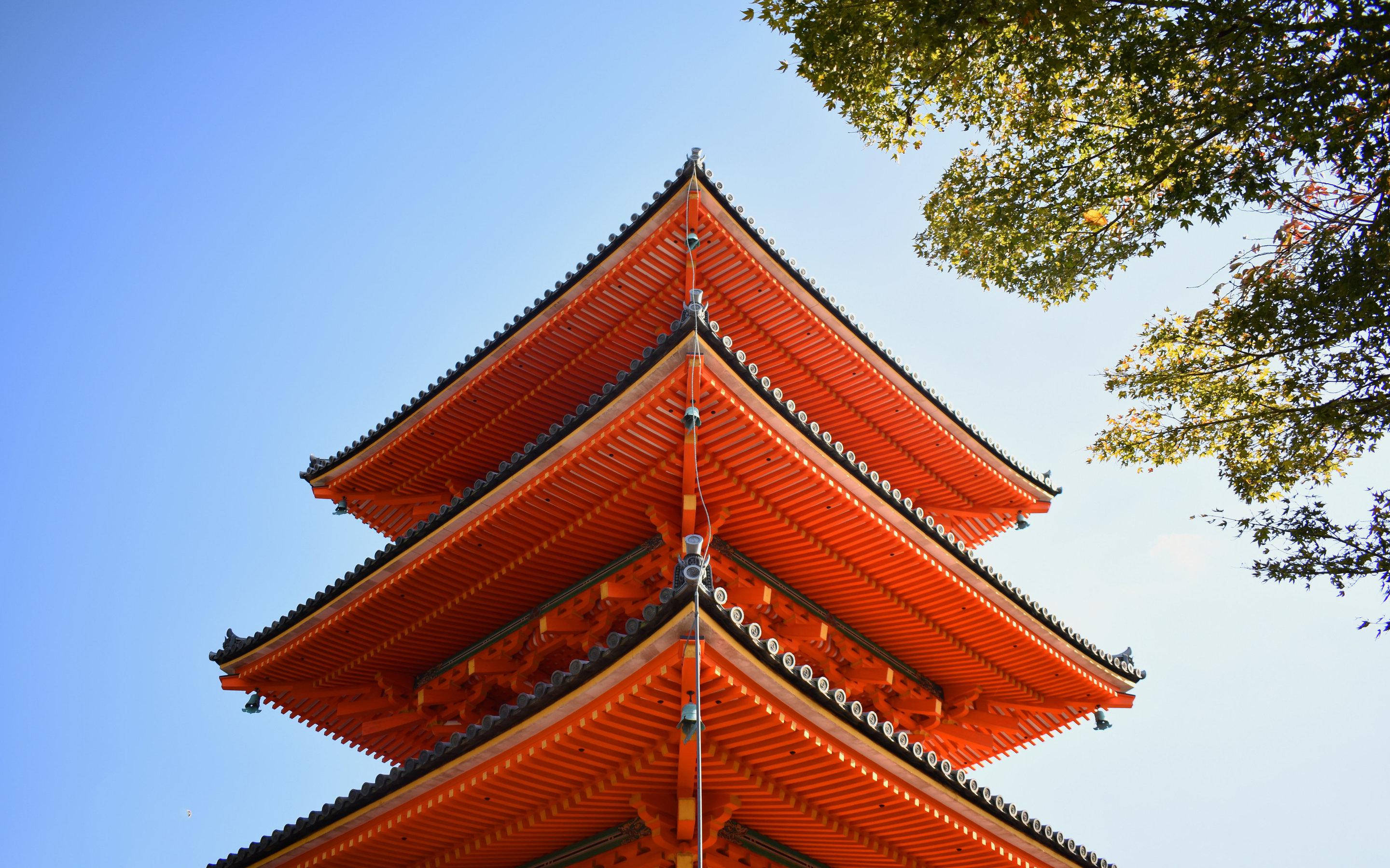 京都 桌布 壁紙 — 一座鮮豔的橙色日本寶塔，層層疊疊的屋頂在藍天白雲和綠樹枝葉的映襯下高聳入雲。