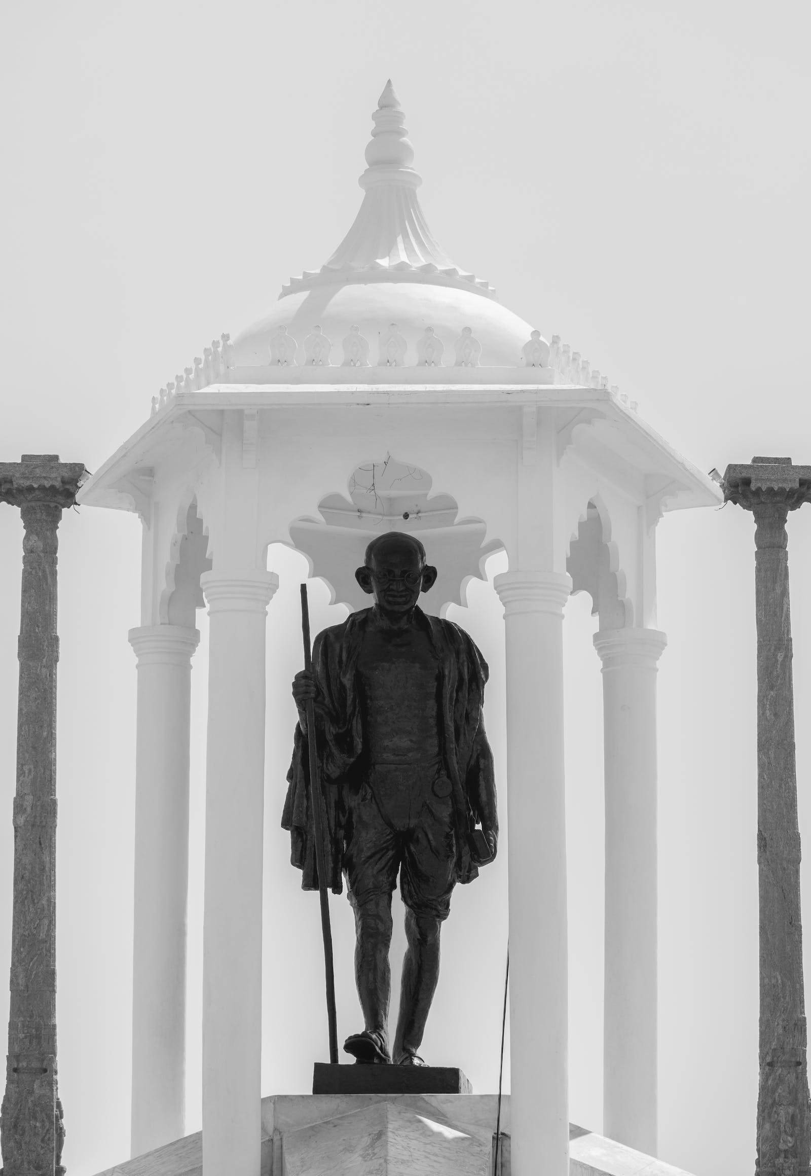 Mahatma Gandhi 桌布 壁紙 — 一座黑白相間的聖雄甘地雕像，莊嚴地矗立在帶有華麗柱子的白色圓頂涼亭下。