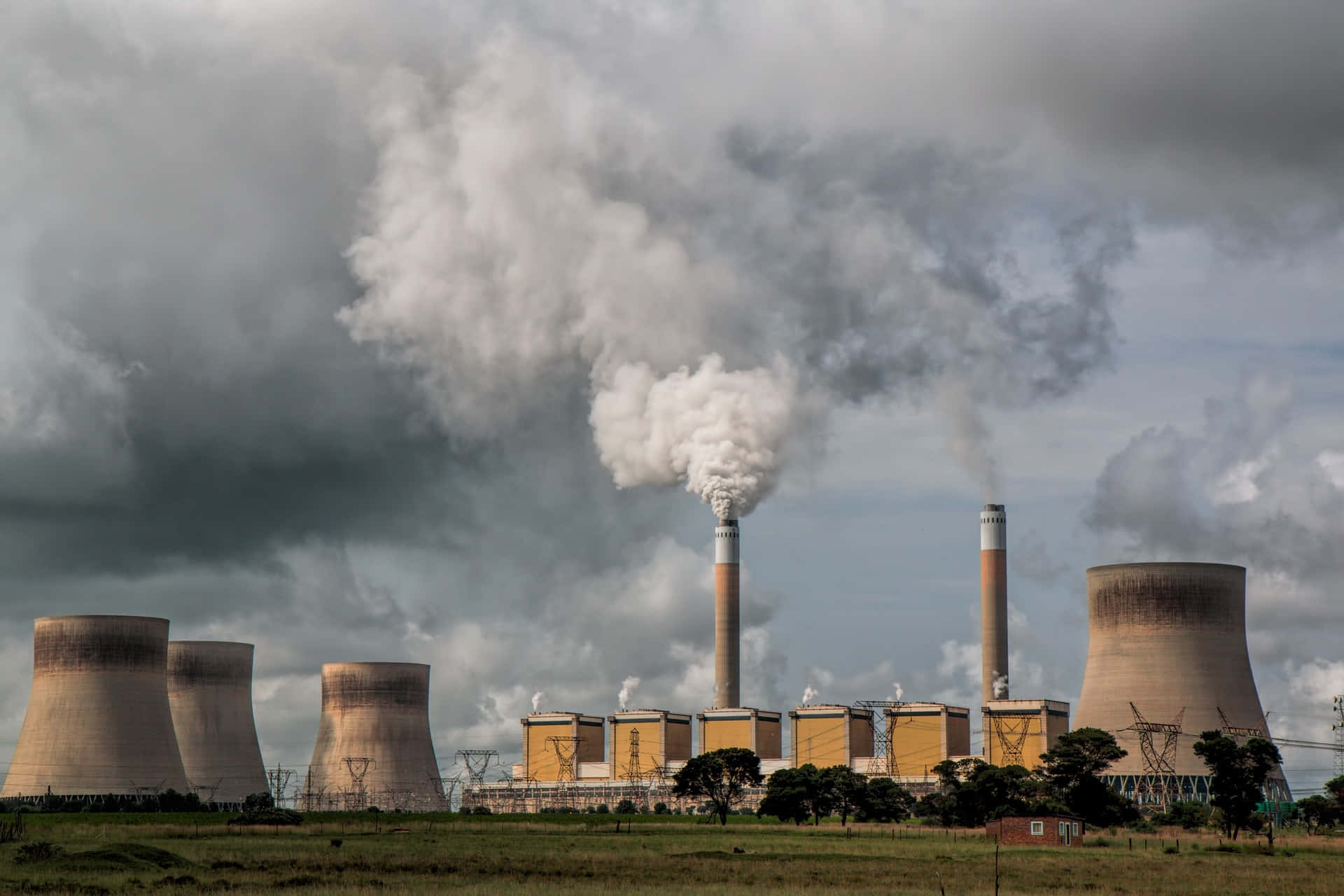 Coal 桌布 壁紙 — 一座龐大的發電廠，冷卻塔和煙囪在戲劇性的多雲天空下排放出濃厚的白色蒸汽。
