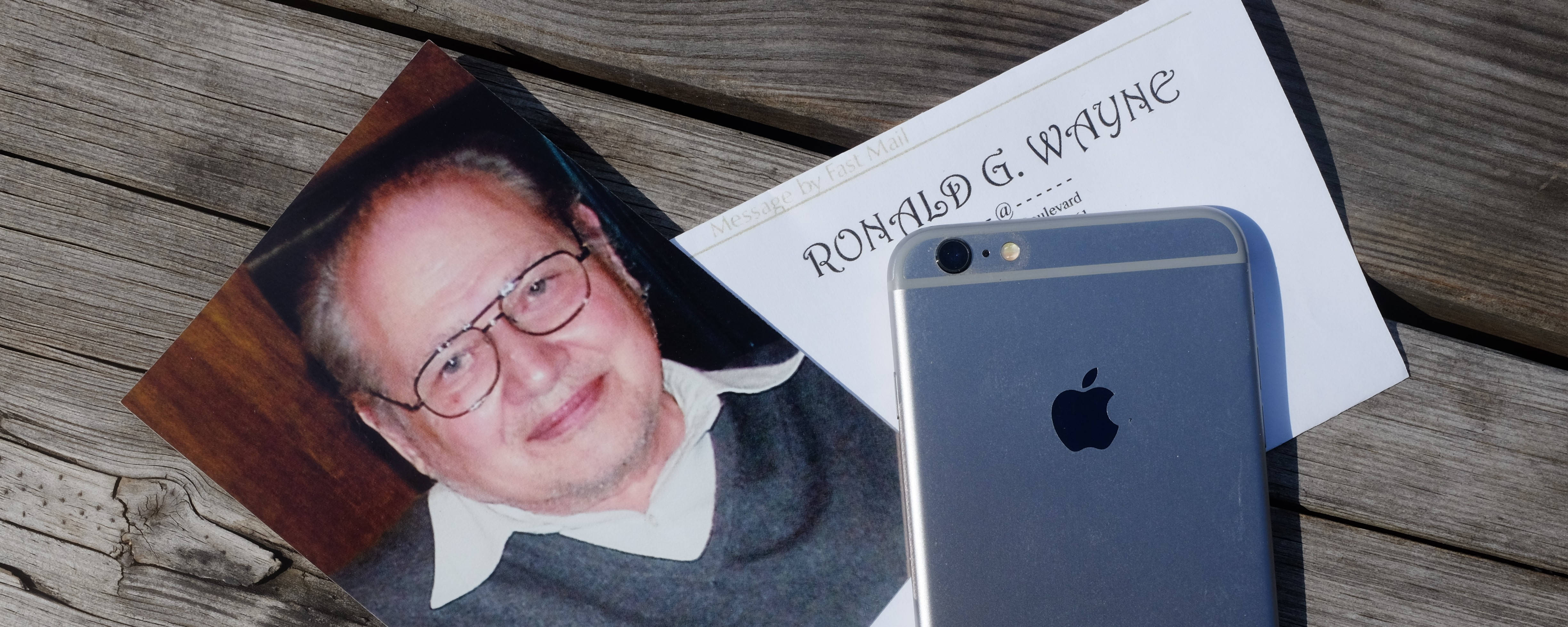 商業 桌布 壁紙 — 一張 Ronald G Wayne 的照片放在風化的木板上，旁邊是一部銀色 iPhone。