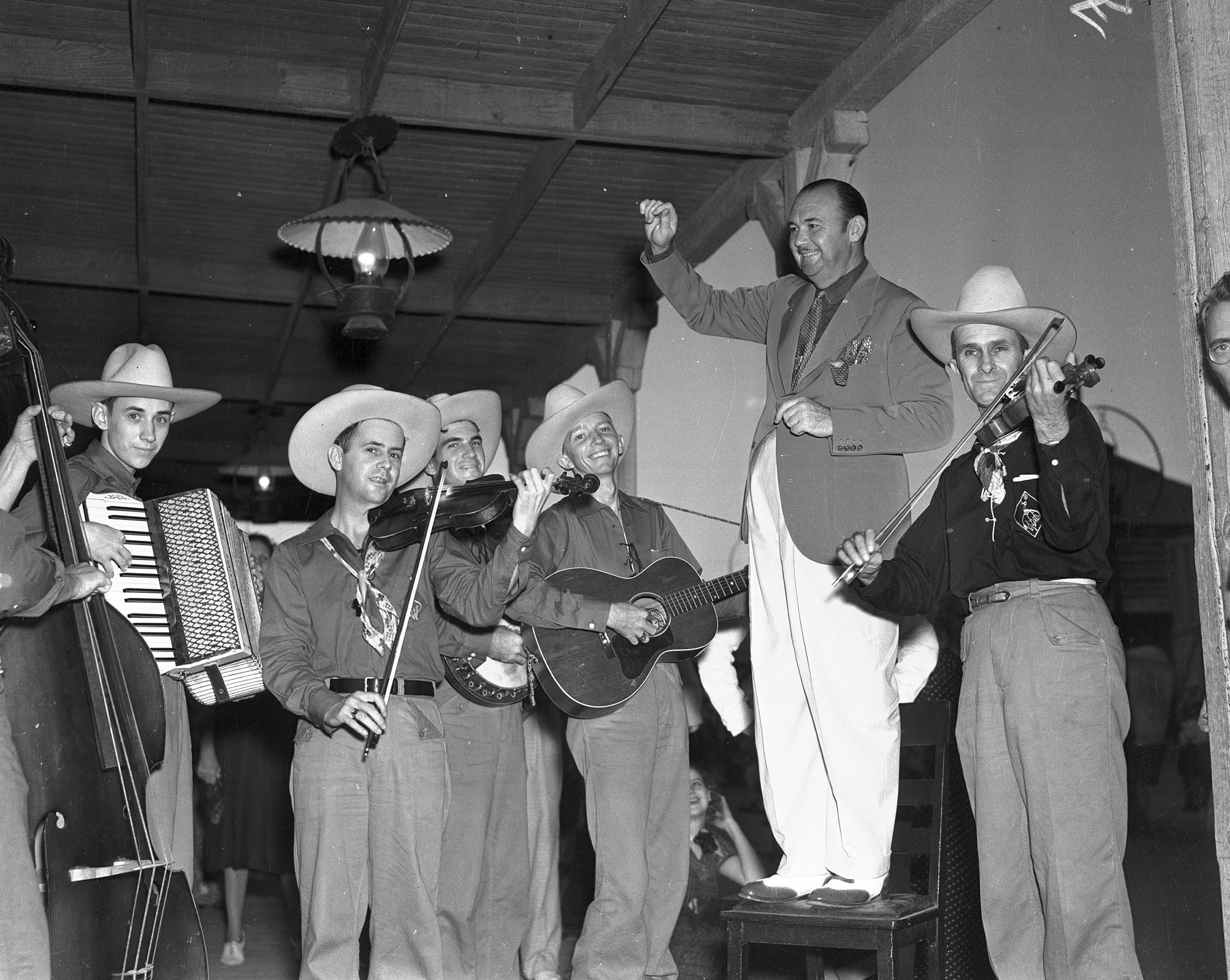 黑白 桌布 壁紙 — 一張1940年代活潑牛仔樂隊在室內演奏吉他、小提琴和手風琴等樂器的黑白照片。
