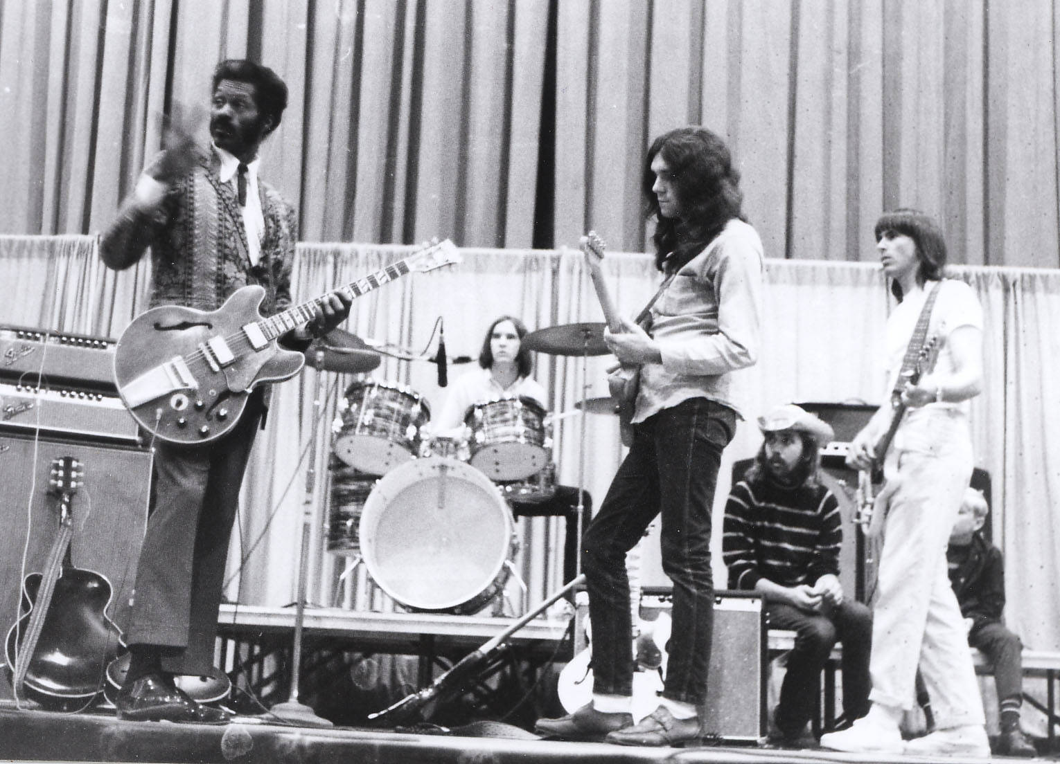 音樂 桌布 壁紙 — 一張1970年代搖滾樂團在舞台上現場表演的黑白照片，配有吉他、鼓和擴音器。