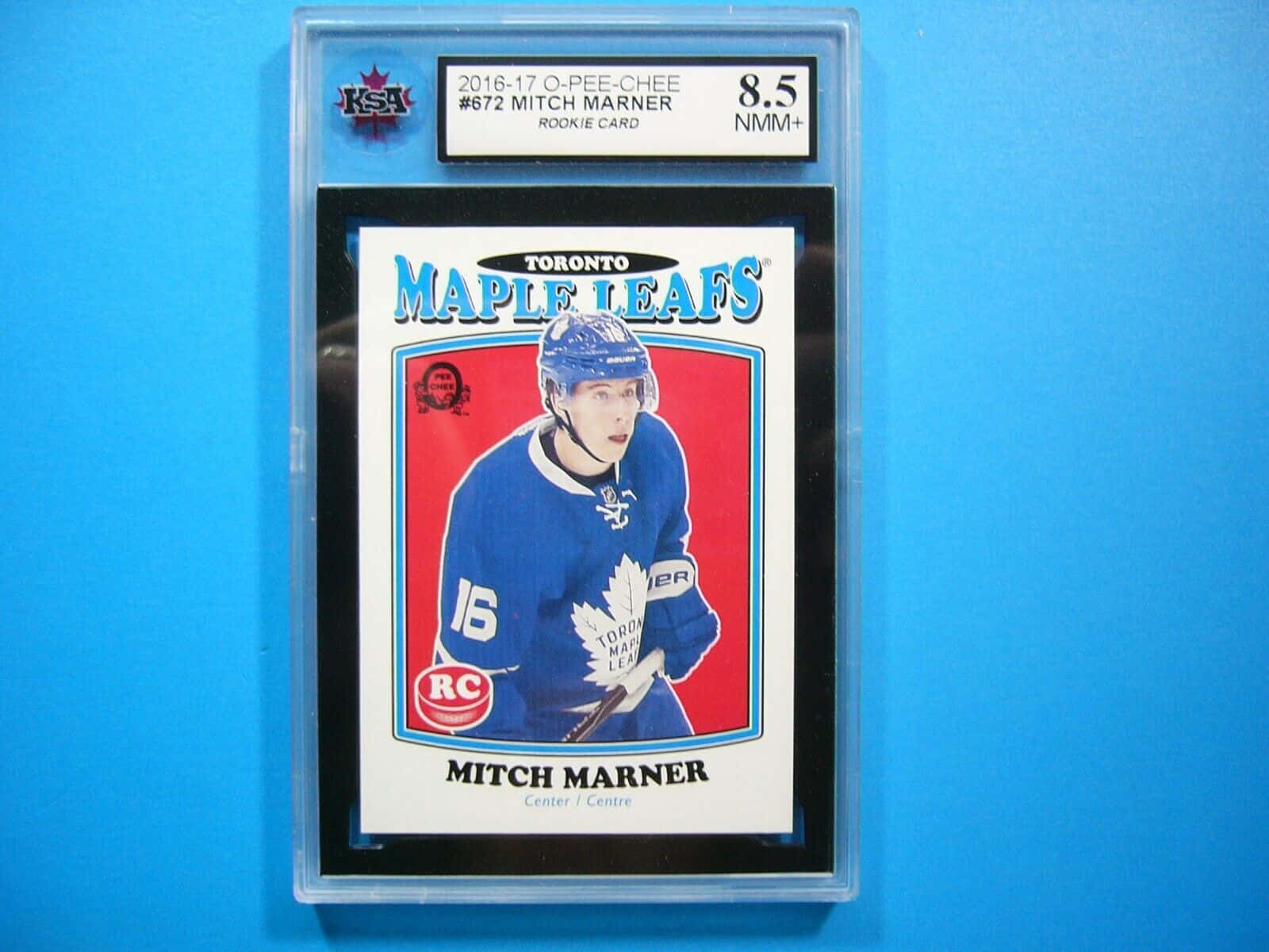 Toronto 桌布 壁紙 — 一張2016-17 O-Pee-Chee米奇·馬納（Mitch Marner）身穿多倫多楓葉隊裝備的新秀曲棍球卡，評級為8.5 NMM+，並展示在透明保護殼中，背景為純藍色。