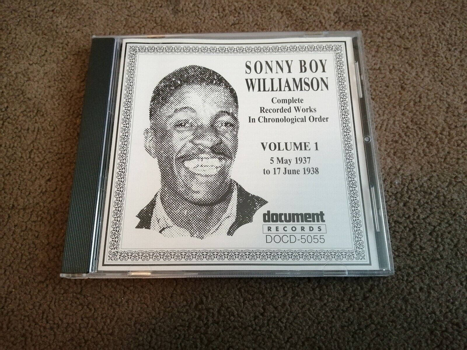 song 桌布 壁紙 — 一張Sonny Boy Williamson Volume 1的復古CD盒放在有紋理的棕色地毯上，帶有半色調肖像和華麗邊框。