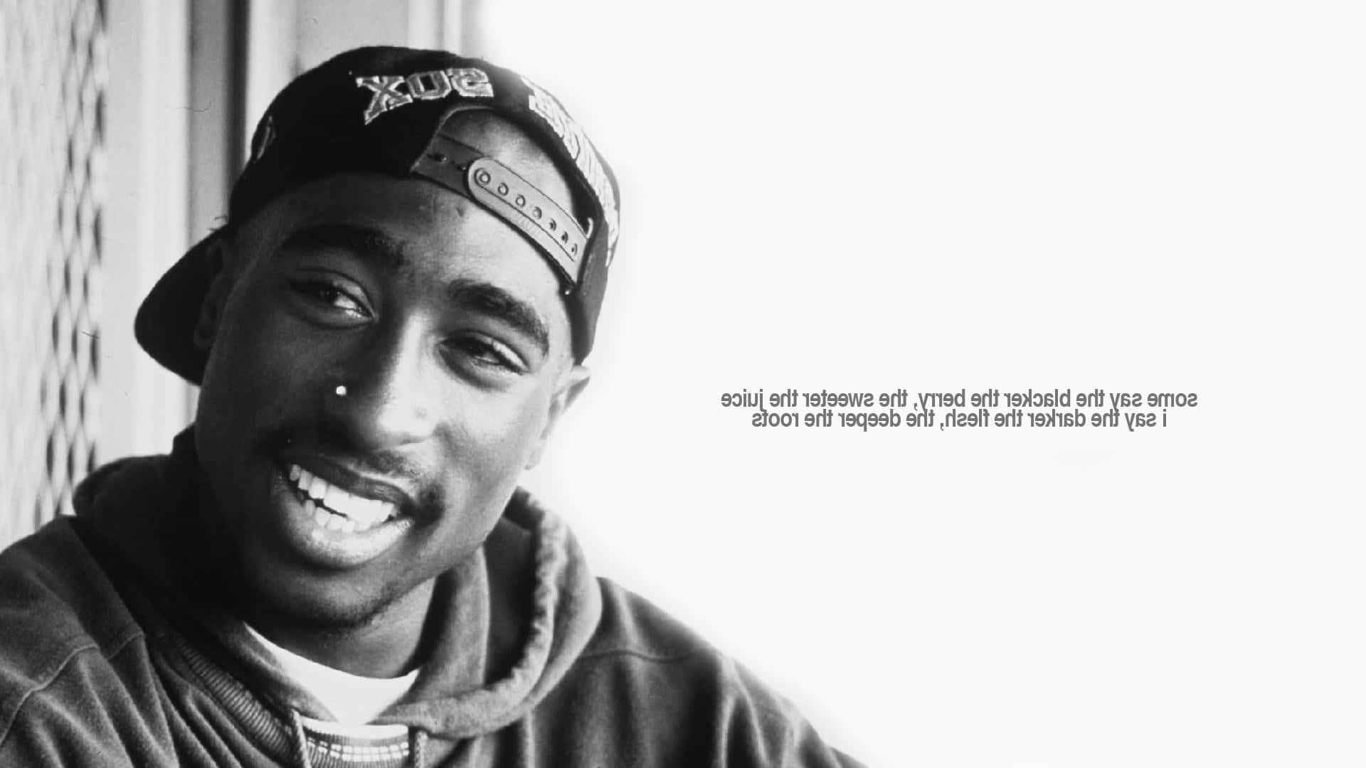  壁紙 — 一張Tupac Shakur的黑白肖像，他戴著向後的帽子和連帽衫，溫暖地微笑，右側有歌詞文字。