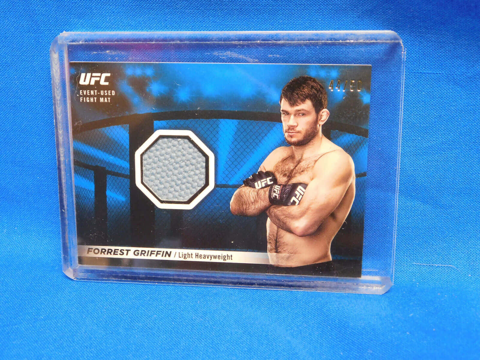 UFC 桌布 壁紙 — 一張UFC收藏卡， featuring Forrest Griffin，附有一塊活動中使用的比賽墊片，背景為藍色布料。