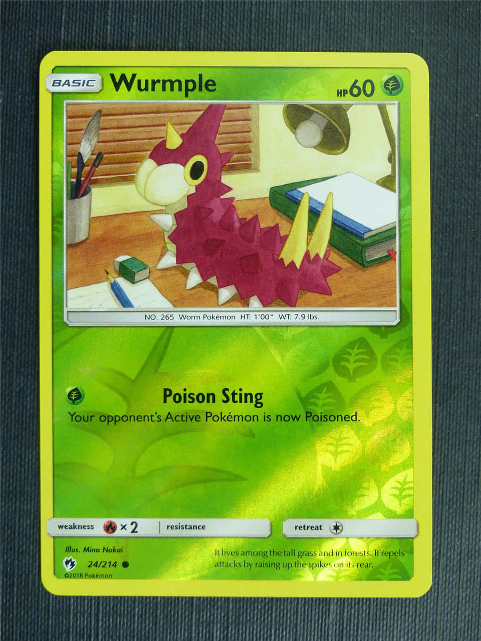 Cards 桌布 壁紙 — 一張Wurmple寶可夢卡，上面有一隻洋紅色的毛蟲生物，放在木桌上，桌上有書本和一盞燈。