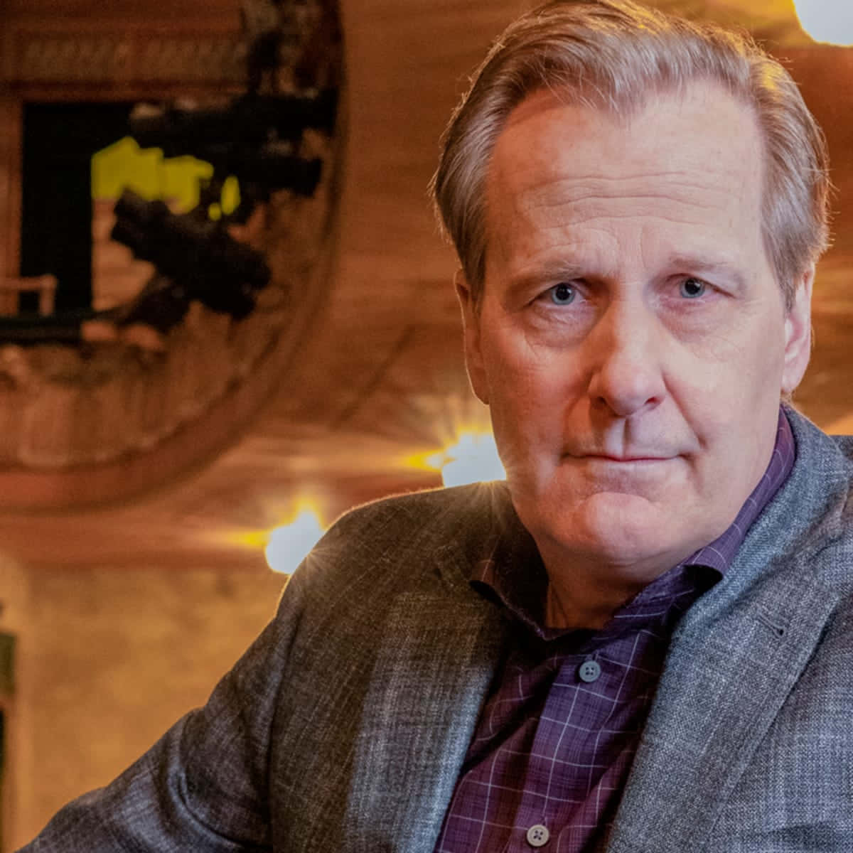 Jeff Daniels 桌布 壁紙 — 一張中年灰髮男子的特寫肖像，他穿著灰色西裝外套和紫色格紋襯衫，背景是溫暖照明的木質室內環境。