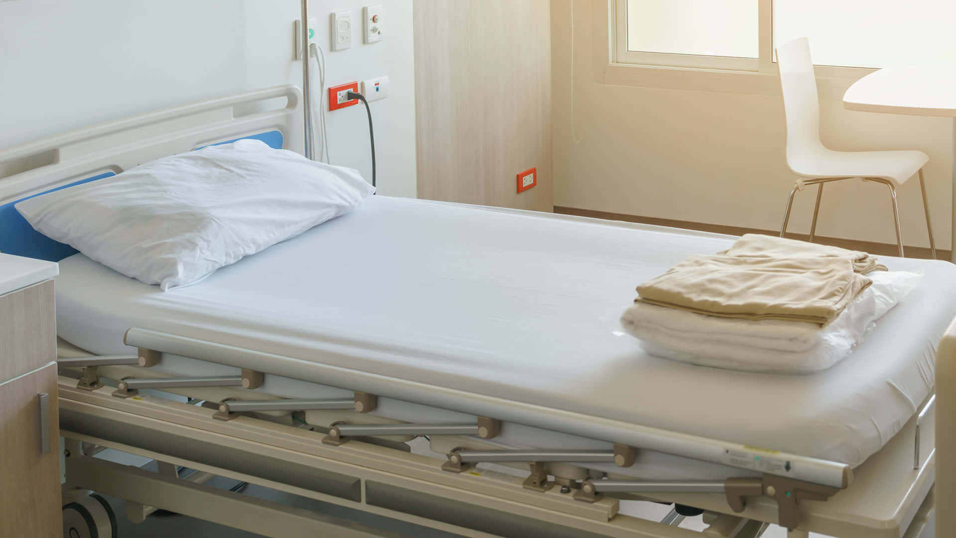 Hospital 桌布 壁紙 — 一張乾淨的醫院病床，配有白色床單和折疊毛巾，位於明亮的臨床房間，內有椅子和窗戶。
