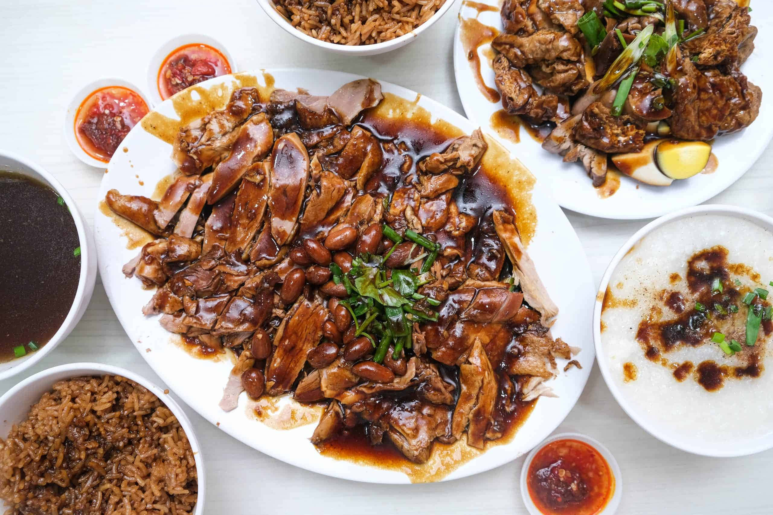Food Photography 桌布 壁紙 — 一張亮白餐桌上，擺放著豐盛的油亮烤鴨配豆類和蔬菜，周圍環繞著飯碗和蘸醬。