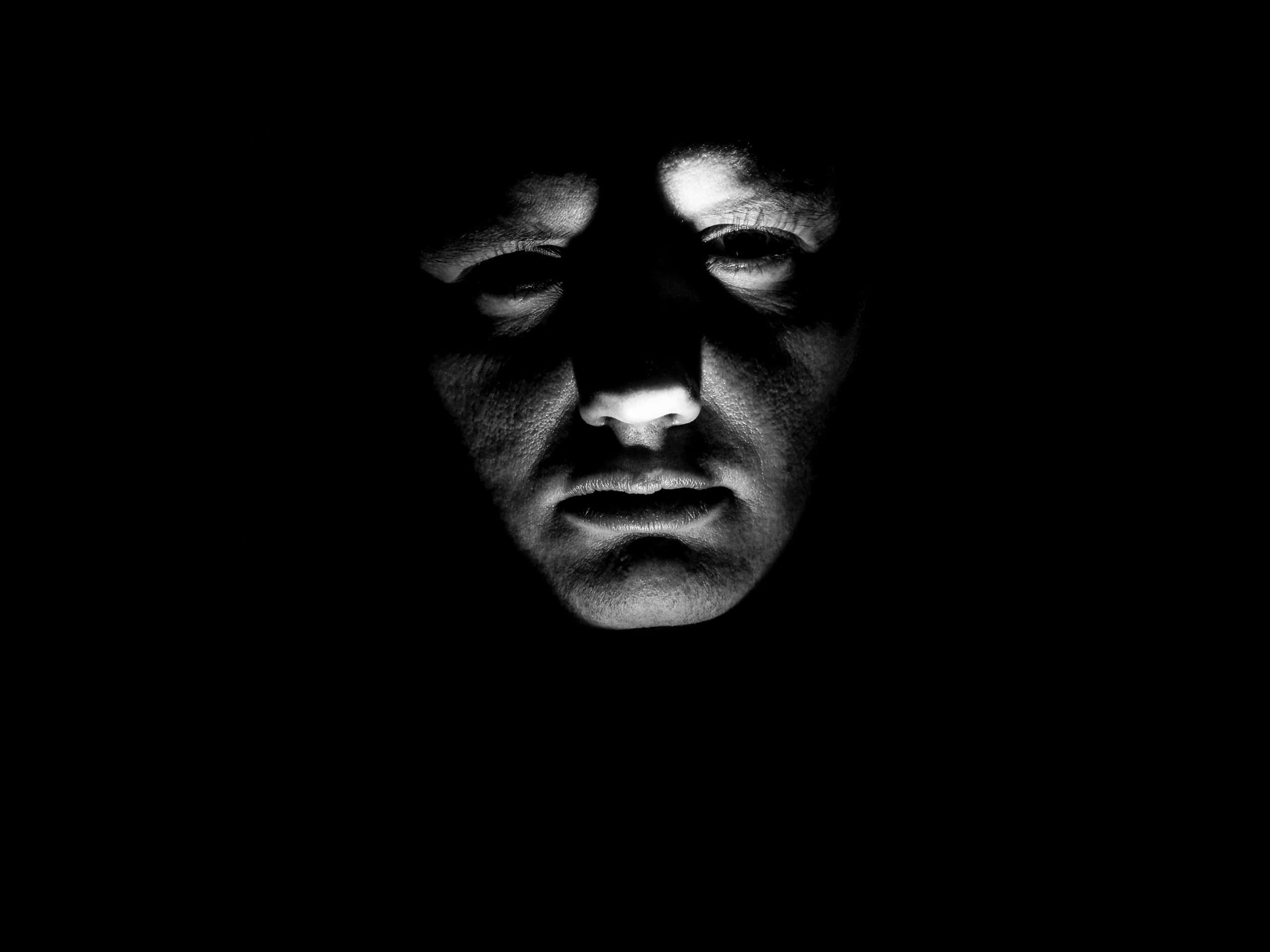 Creepy Halloween 桌布 壁紙 — 一張令人毛骨悚然的人臉從黑暗中浮現，強烈的明暗對比光線突顯出銳利的眼睛和嘴唇。