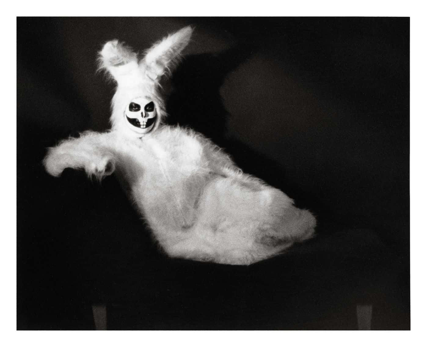 Creepy Easter Bunny 桌布 壁紙 — 一張令人毛骨悚然的黑白照片，展示了一個毛茸茸的兔子服裝，上面畫著骷髏臉，背景是黑暗的。