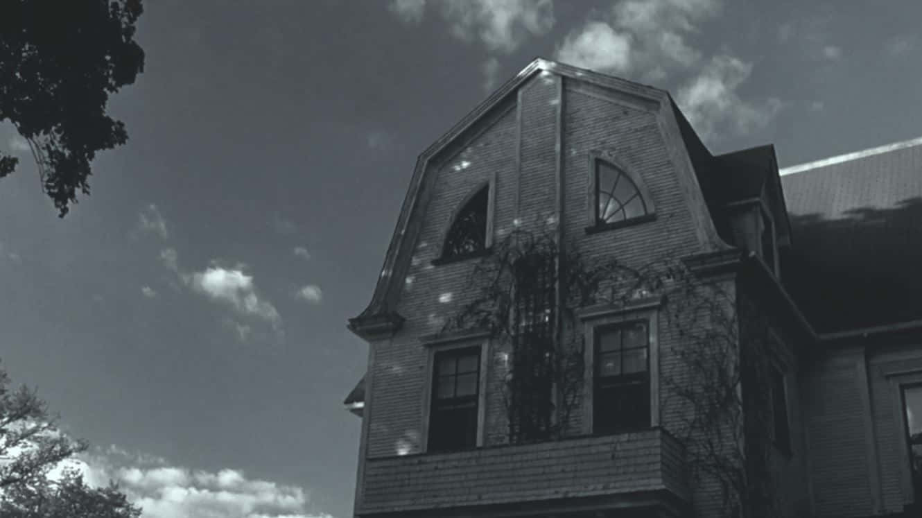 Haunted House 桌布 壁紙 — 一張令人毛骨悚然的黑白照片，拍攝了一棟舊磚房，牆上爬滿了常春藤，天空多雲。