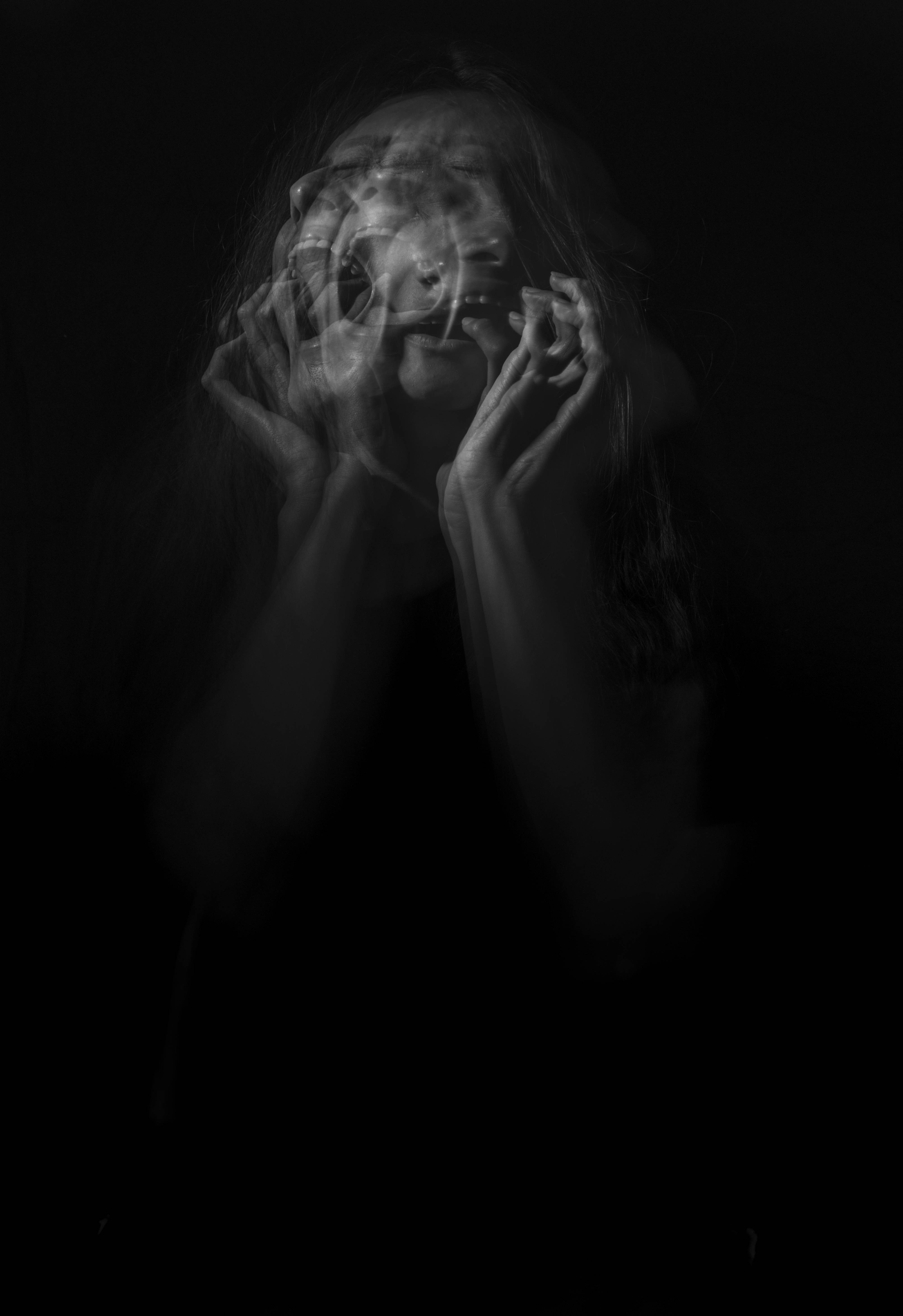 Anxiety 桌布 壁紙 — 一張令人難忘的黑白肖像，人物雙手靠近臉部，在黑暗背景上呈現幽靈般的雙重曝光效果。