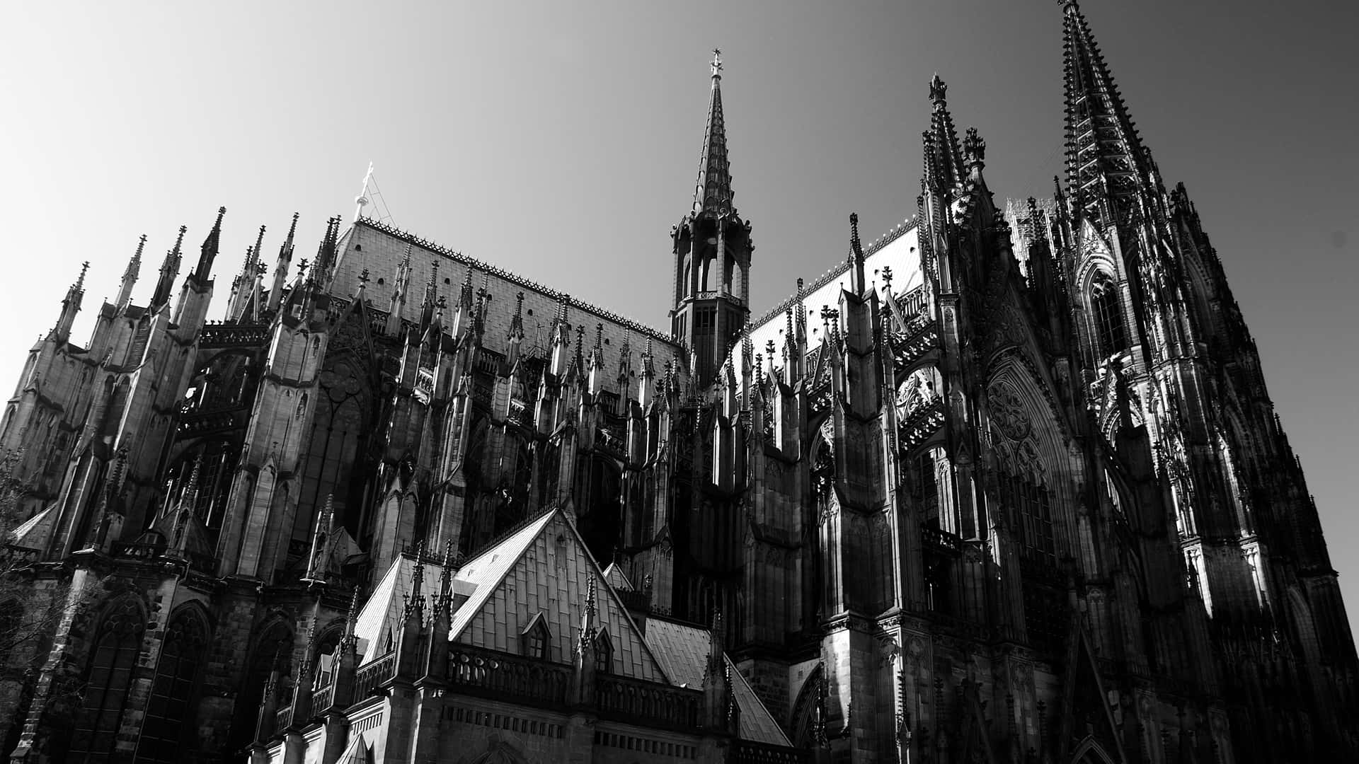 Catholic Desktop 桌布 壁紙 — 一張以低角度拍攝的戲劇性黑白照片，展現一座高聳的哥德式大教堂，其精緻的尖塔和尖拱門在晴朗的天空下格外突出。