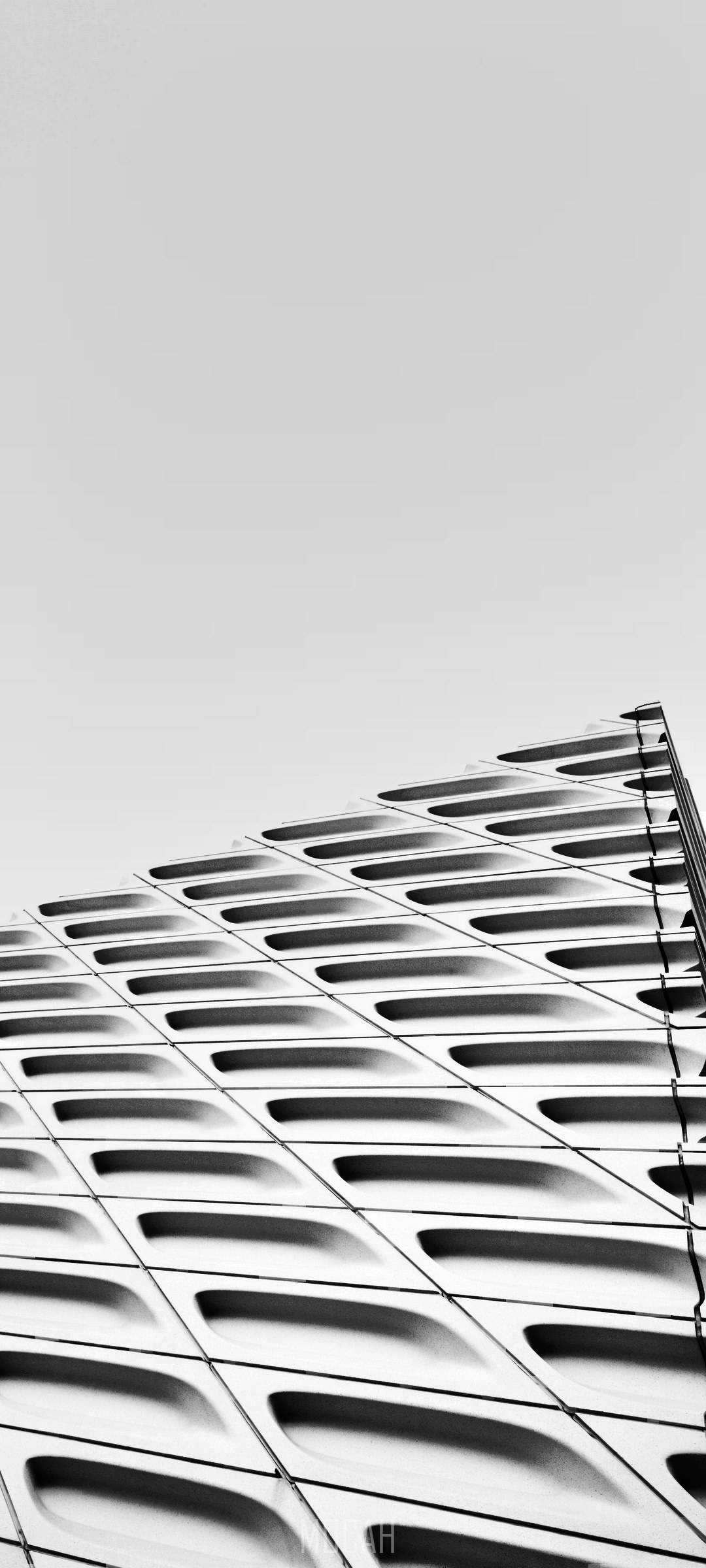 建築 桌布 壁紙 — 一張以低角度拍攝的現代建築幾何外牆單色照片，背景是淡色的天空。