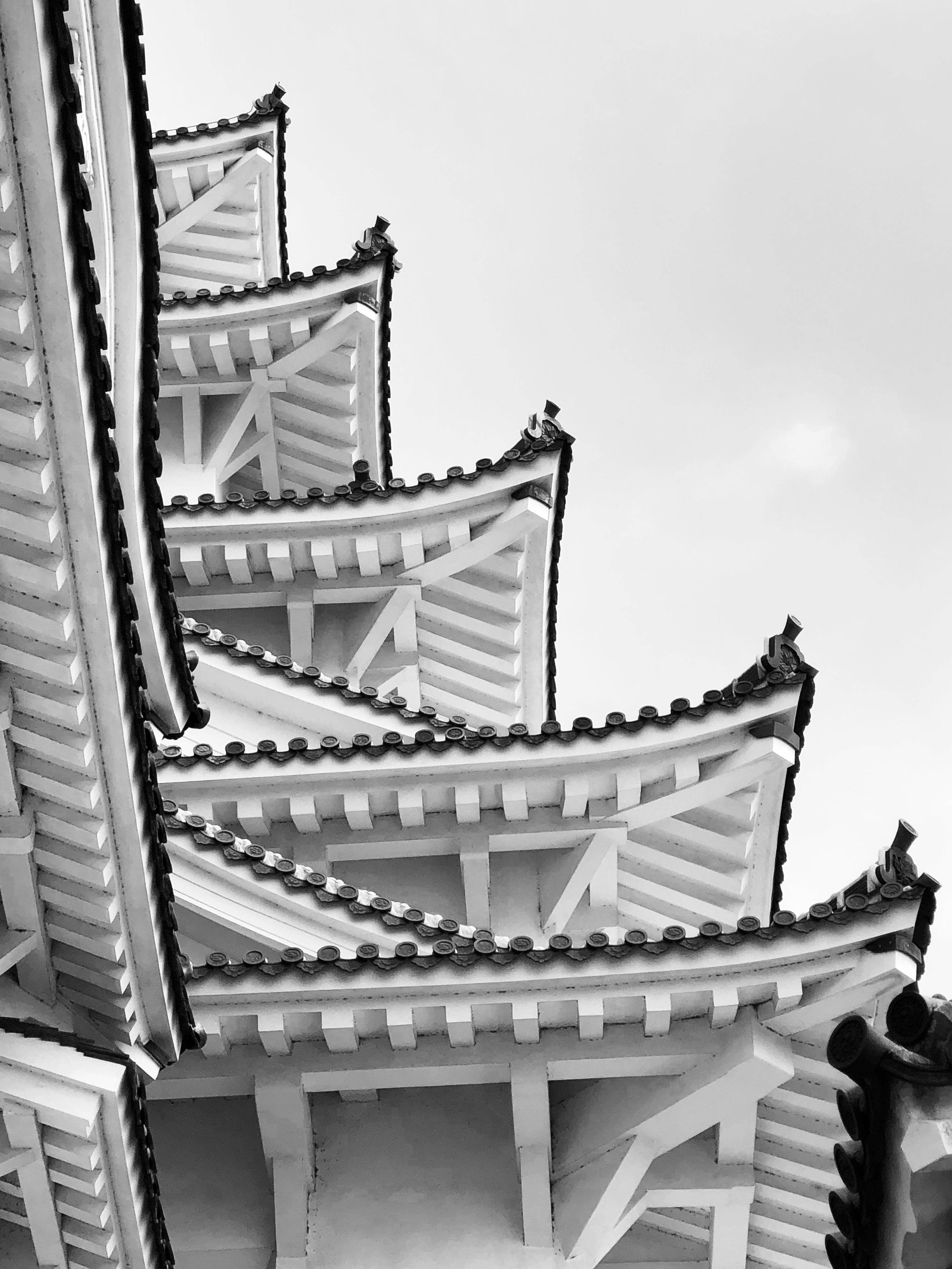 Himeji Castle 桌布 壁紙 — 一張以淡色天空為背景，低角度拍攝的傳統日本寺廟屋頂層次黑白照片，效果引人注目。