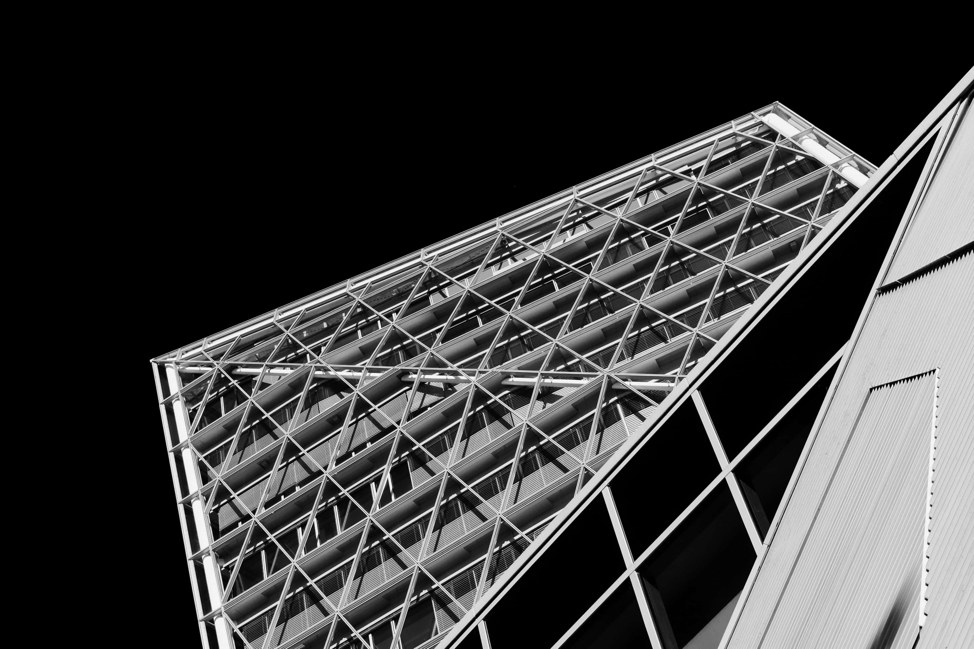 Black And White Architecture 桌布 壁紙 — 一張以純黑天空為背景，從低角度拍攝的現代建築幾何金屬格柵外牆的清晰黑白照片。