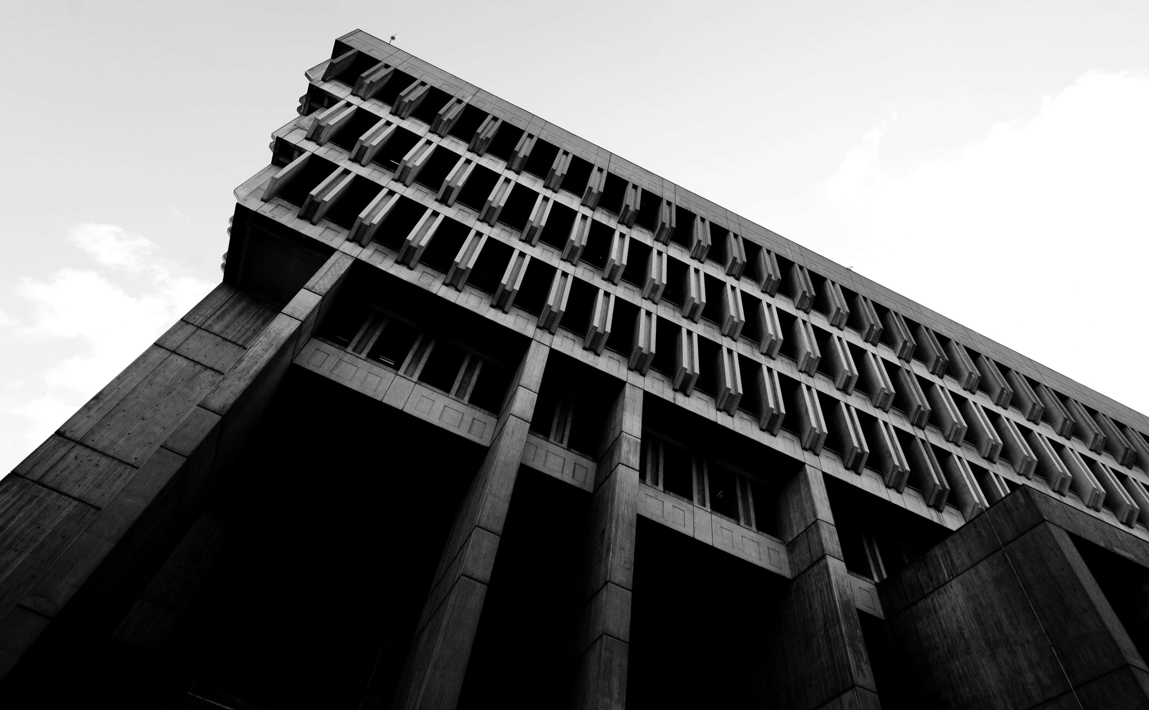 Black And White City 桌布 壁紙 — 一張以黑白低角度拍攝的粗獷主義混凝土建築物照片，具有幾何圖案和深沉的陰影。