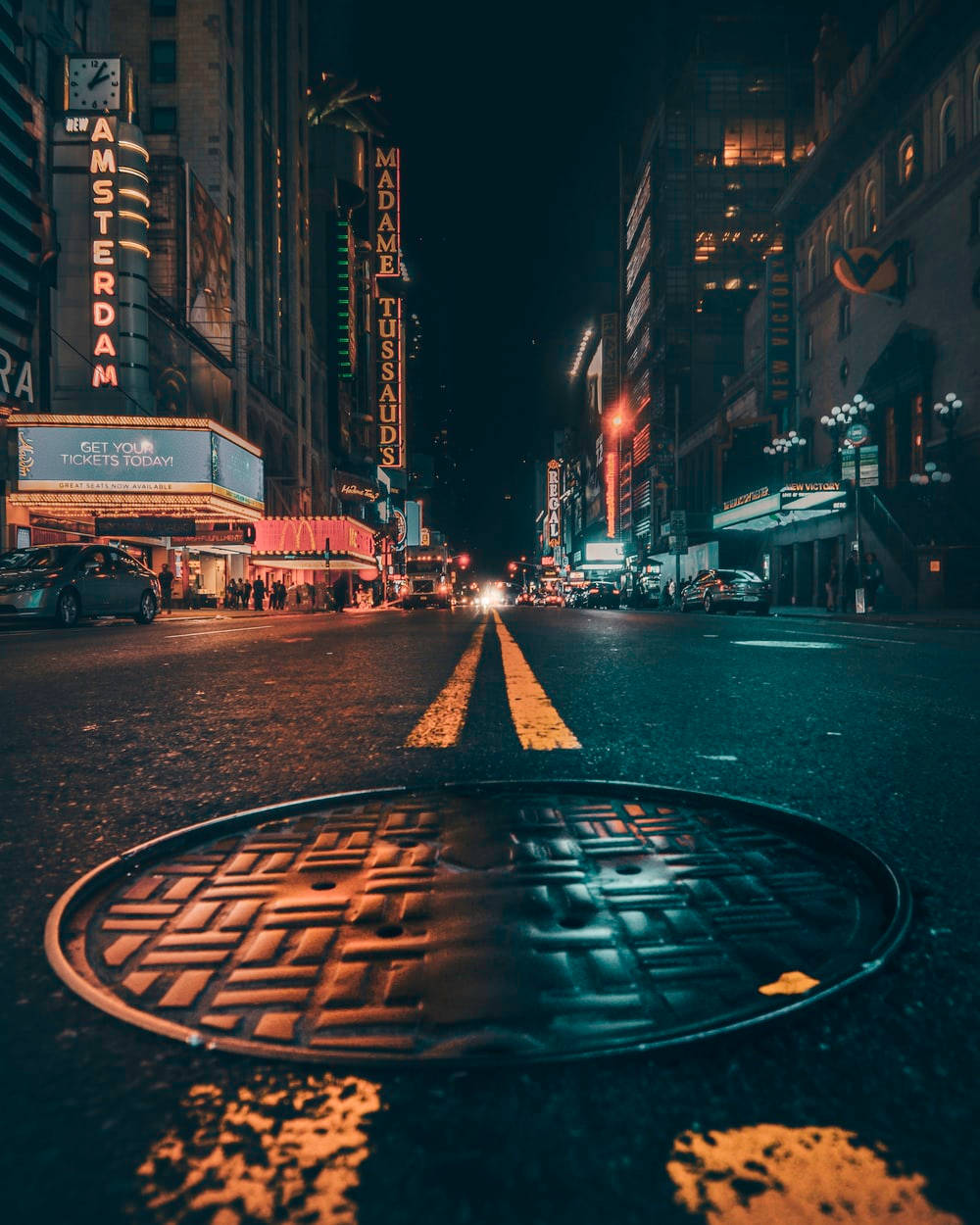 City At Night 桌布 壁紙 — 一張低角度夜拍，濕漉漉的城市街道，前景是人孔蓋，還有來自杜莎夫人蠟像館和阿姆斯特丹劇院的霓虹燈招牌。