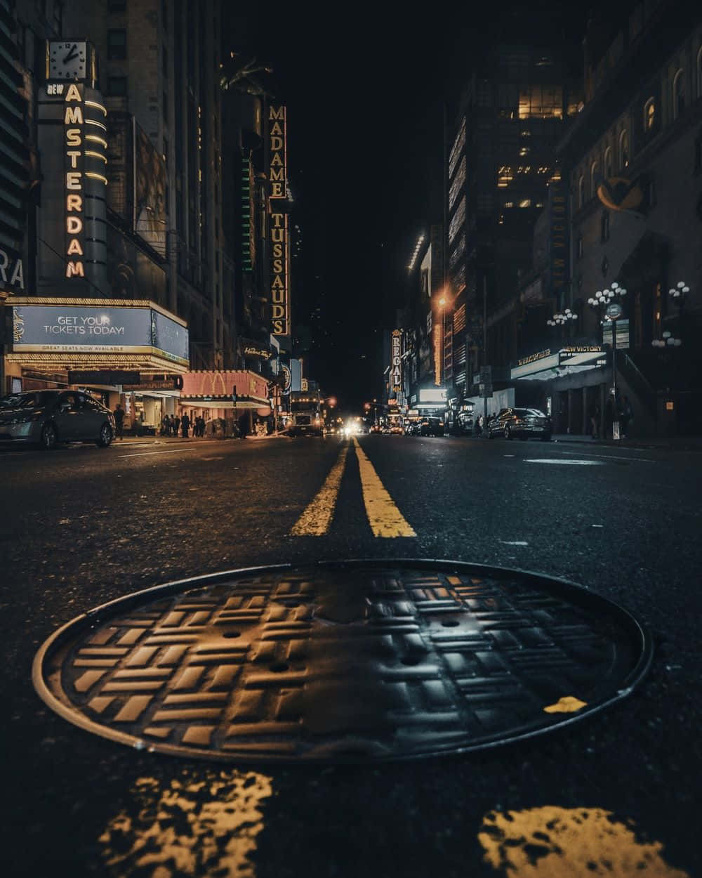 夜景城市 桌布 壁紙 — 一張低角度夜間拍攝的濕漉漉城市街道照片，前景有沙井蓋，以及杜莎夫人蠟像館和阿姆斯特丹劇院的發光霓虹燈招牌。