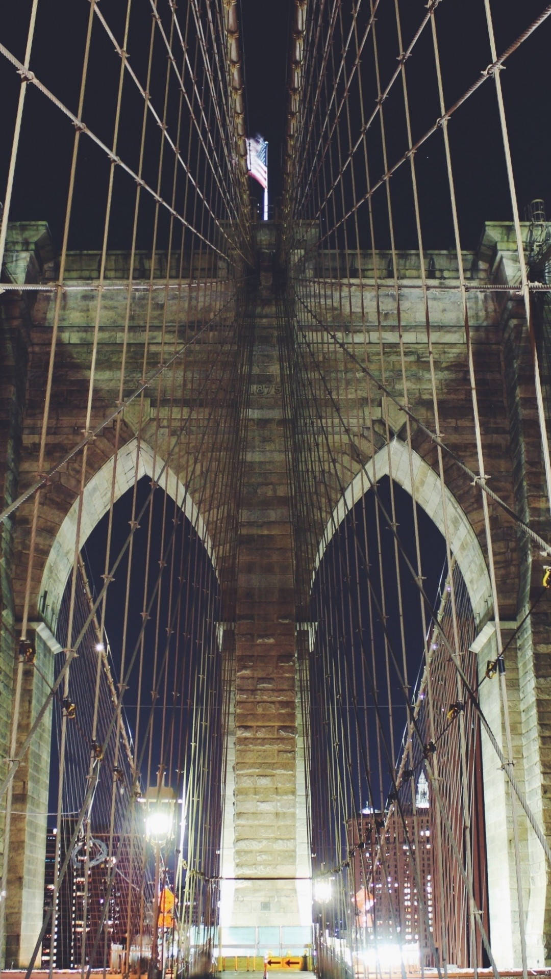 Brooklyn Bridge 桌布 壁紙 — 一張低角度拍攝的戲劇性夜景，布魯克林大橋的石塔和發光的懸索在黑暗的天空下。