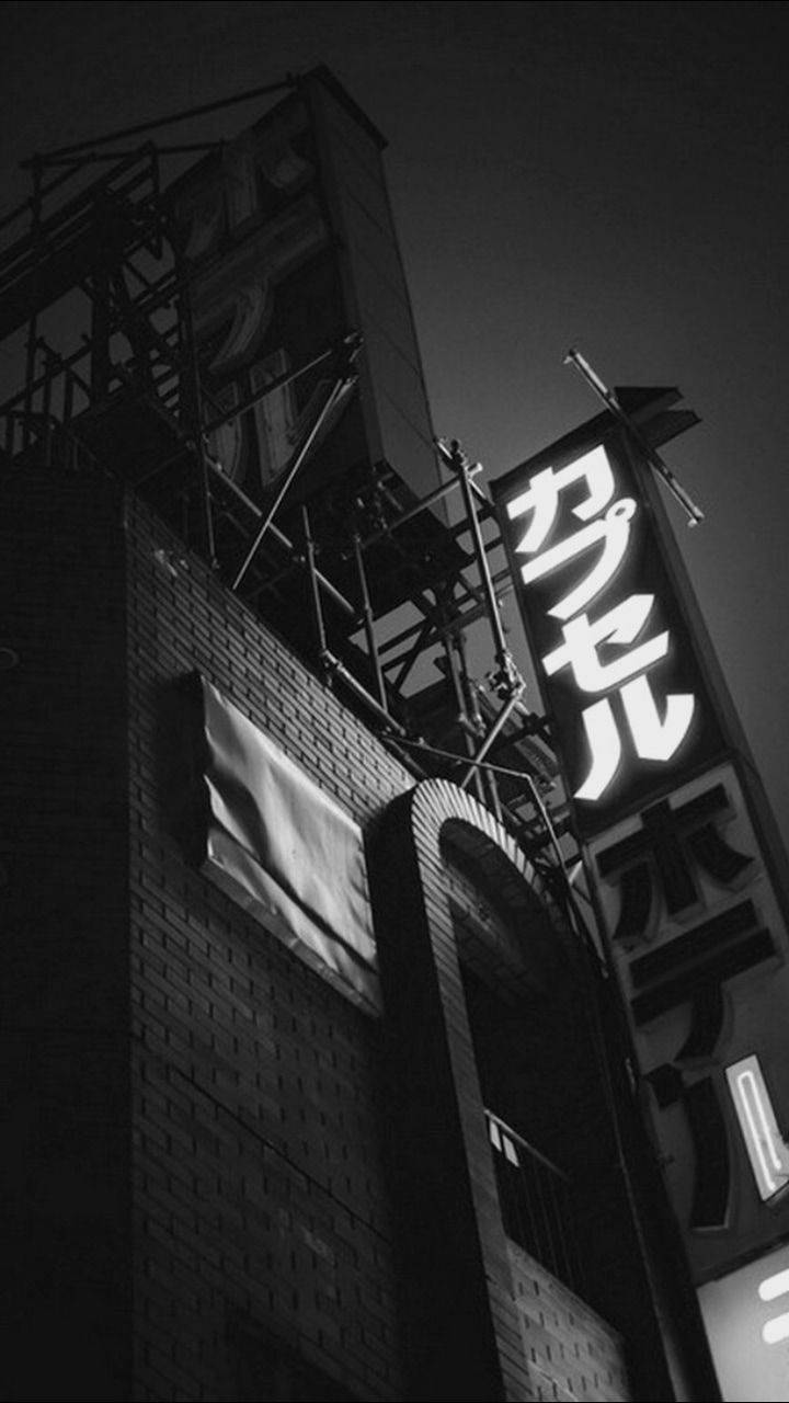 黑色美學手機 桌布 壁紙 — 一張低角度黑白照片，拍攝夜間磚砌建築上發光的霓虹燈招牌，上方有鷹架。
