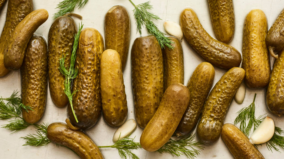 Pickle 桌布 壁紙 — 一張俯拍照片，閃亮的醃黃瓜上撒有蒔蘿和蒜瓣，放在淺色木質表面上。