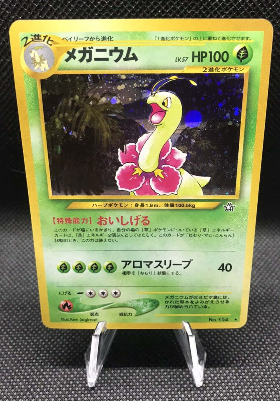 任天堂 桌布 壁紙 — 一張充滿活力的Mega Bayleef Pokémon卡，特徵是一隻黃色生物帶有粉紅色花瓣，直立展示在透明支架上，背景為深色紋理。