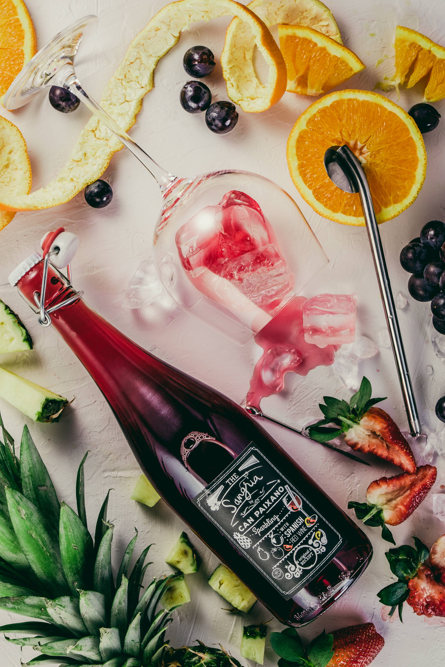 drinking wine 桌布 壁紙 — 一張充滿活力的俯拍照片，展示一個紅色氣泡飲料瓶，冰塊和柑橘類水果藝術地排列在淺色表面上。
