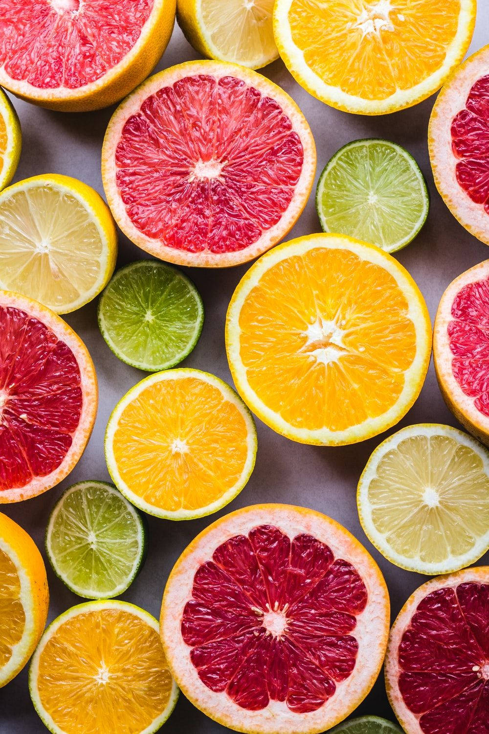 Fruits 桌布 壁紙 — 一張充滿活力的俯拍照片，展示了各種切片柑橘類水果，包括葡萄柚、檸檬、萊姆和柳橙，排列在中性表面上。