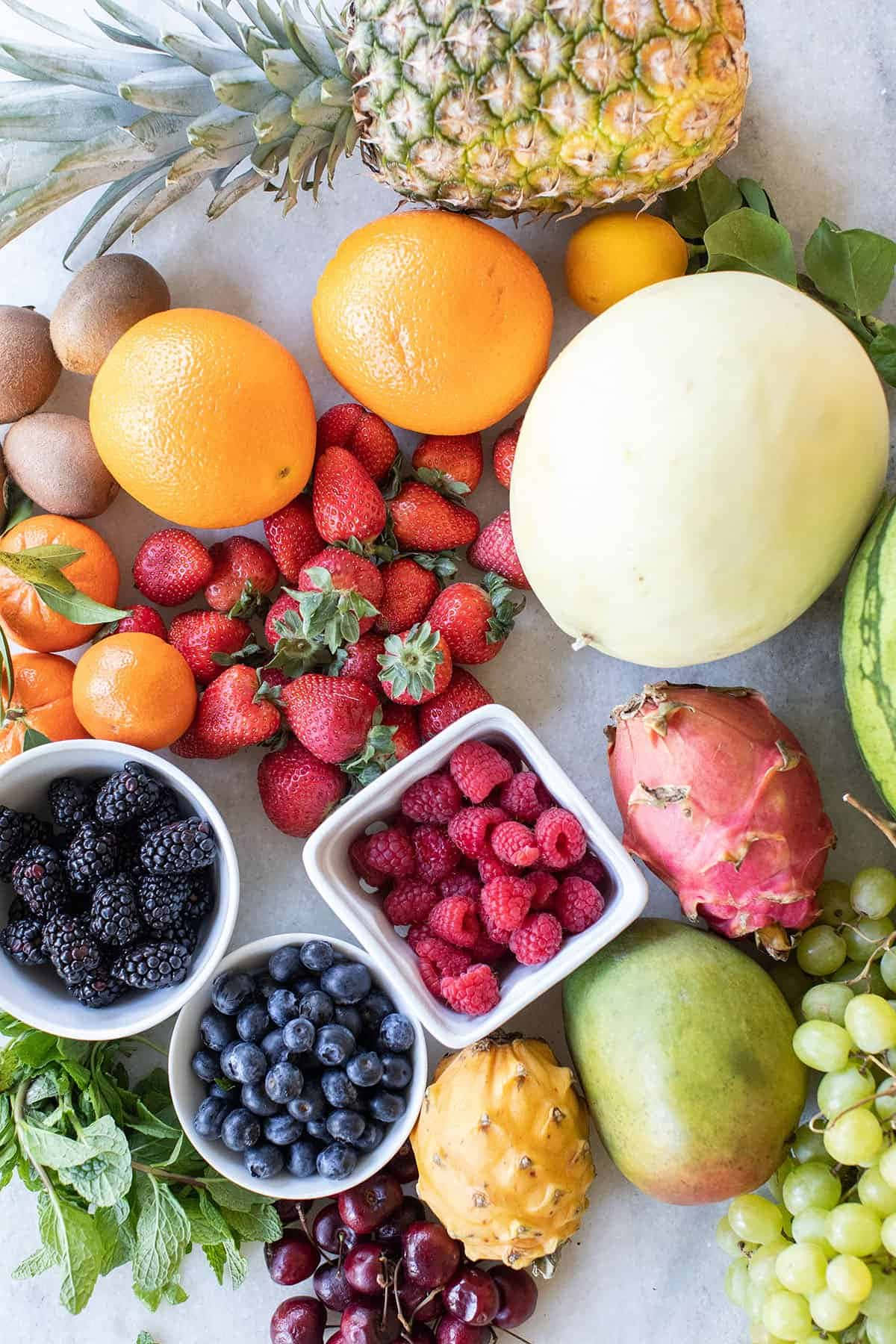 Fruit 桌布 壁紙 — 一張充滿活力的俯拍照片，展示各種新鮮水果，包括鳳梨、柳橙、草莓、覆盆子和葡萄，排列在淺色表面上。