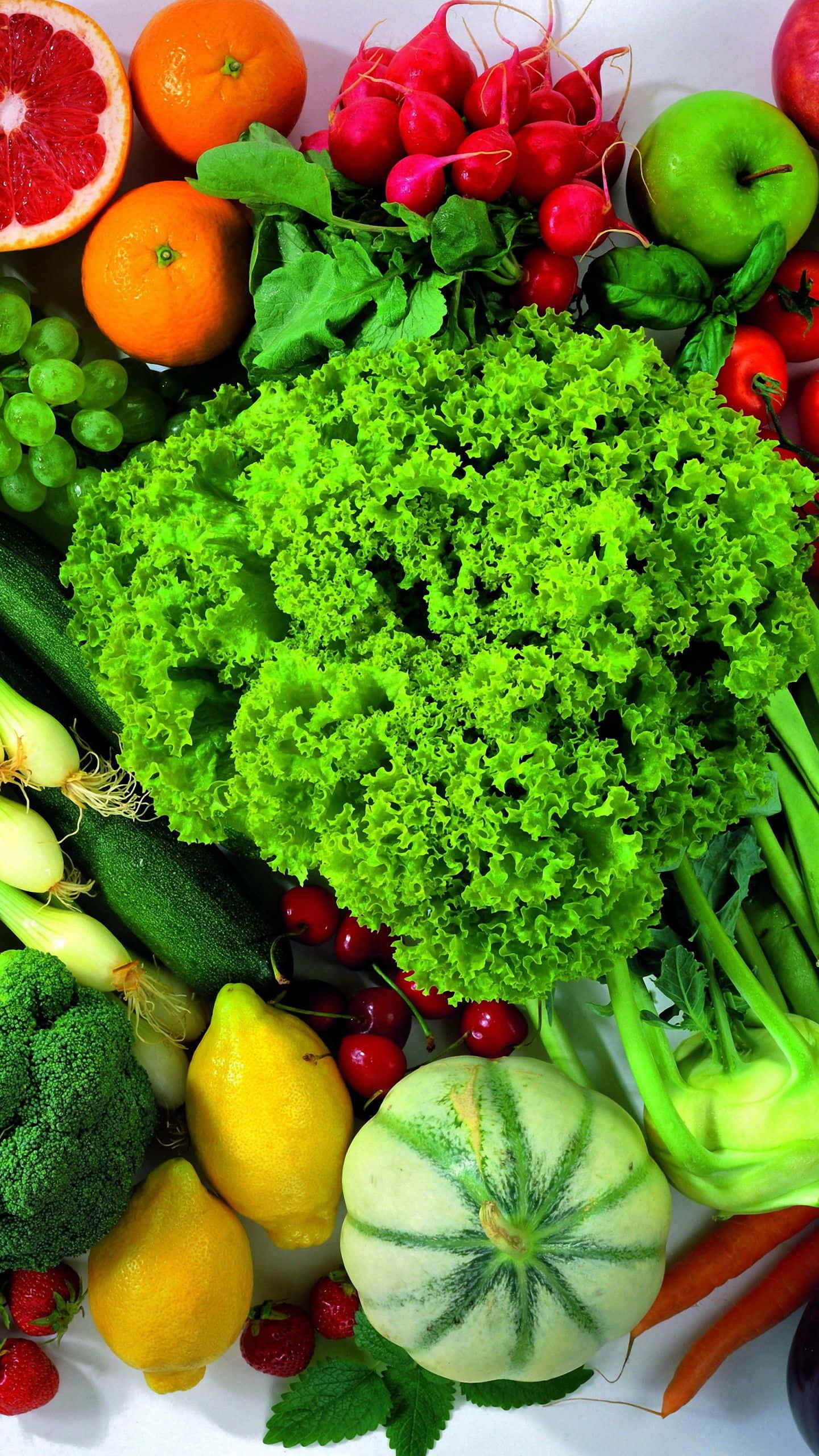 Vegetable 桌布 壁紙 — 一張充滿活力的俯拍照片，展示各種新鮮水果和蔬菜，包括生菜、葡萄、橙子和蘿蔔，排列在白色表面上。